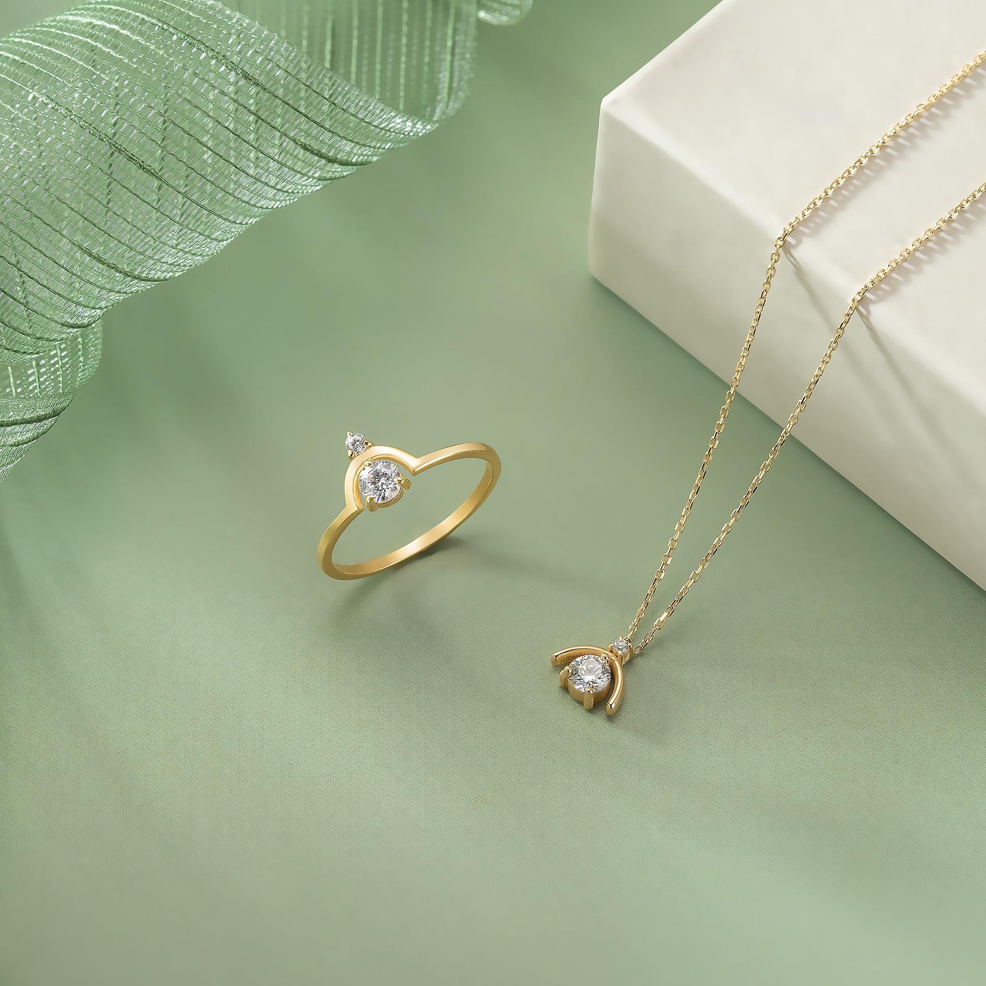 a gold ring and necklace with a pendant on a green background.