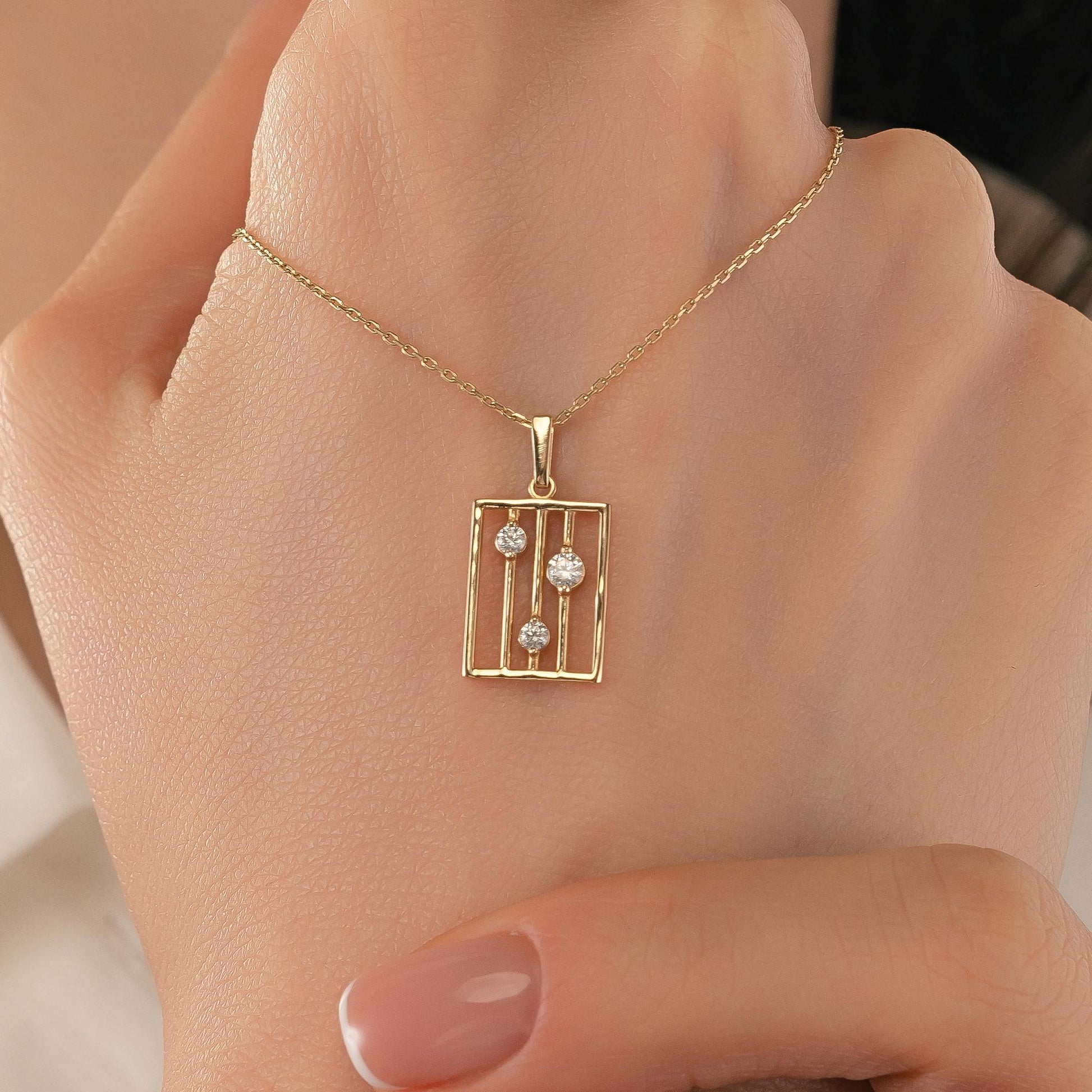 A gold necklace with a pendant featuring a rectangular design with two small diamonds set in a cage-like structure.