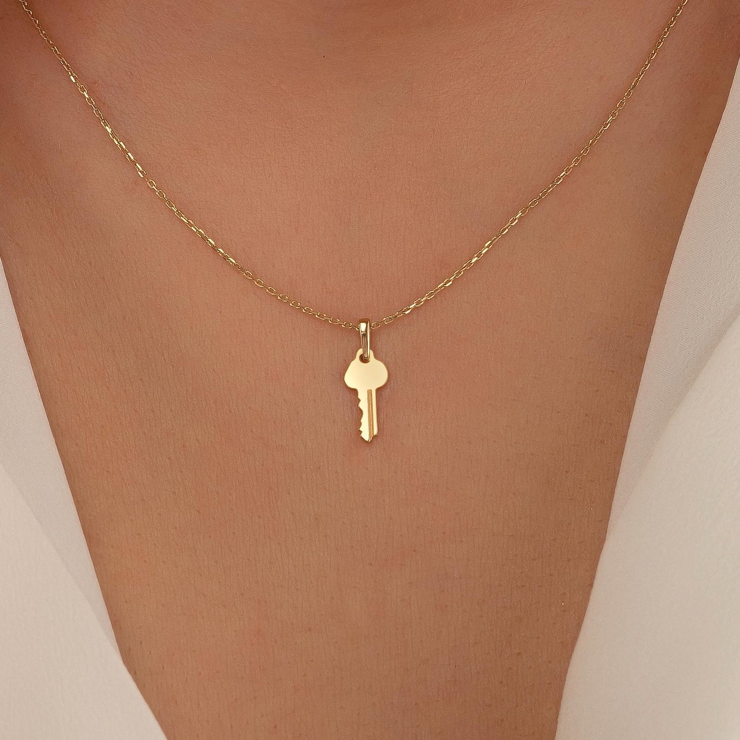 A gold-colored necklace with a small key pendant is shown on a person's neck.