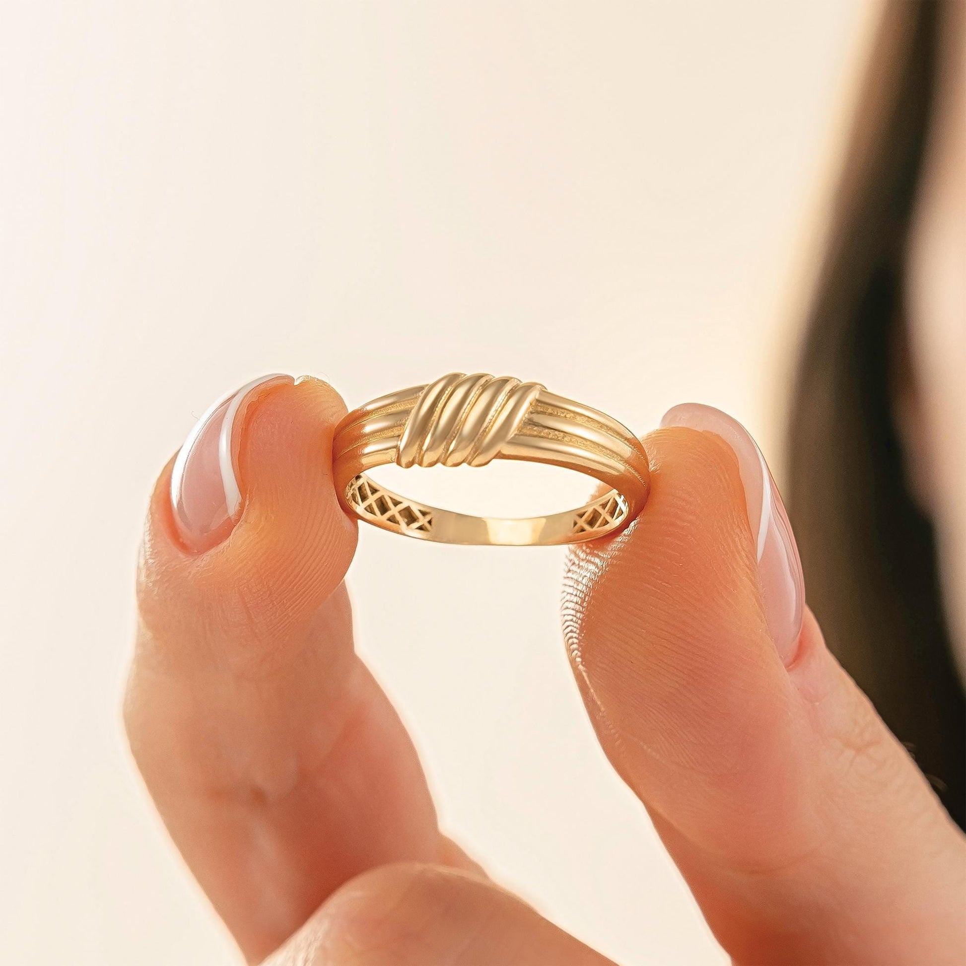 A person's hand holding a gold ring with a twisted design.