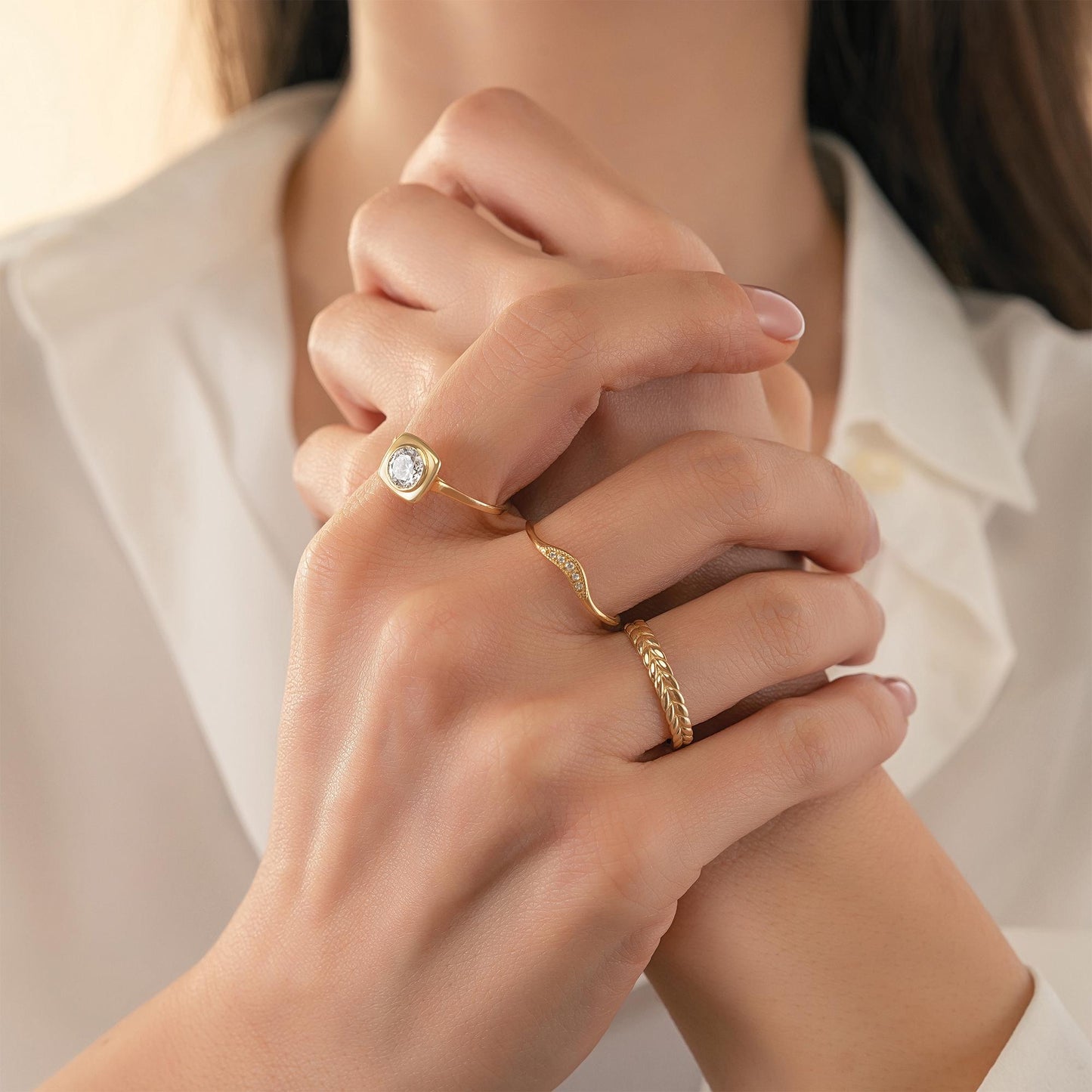 A close-up of a person's hands wearing three gold rings on different fingers.