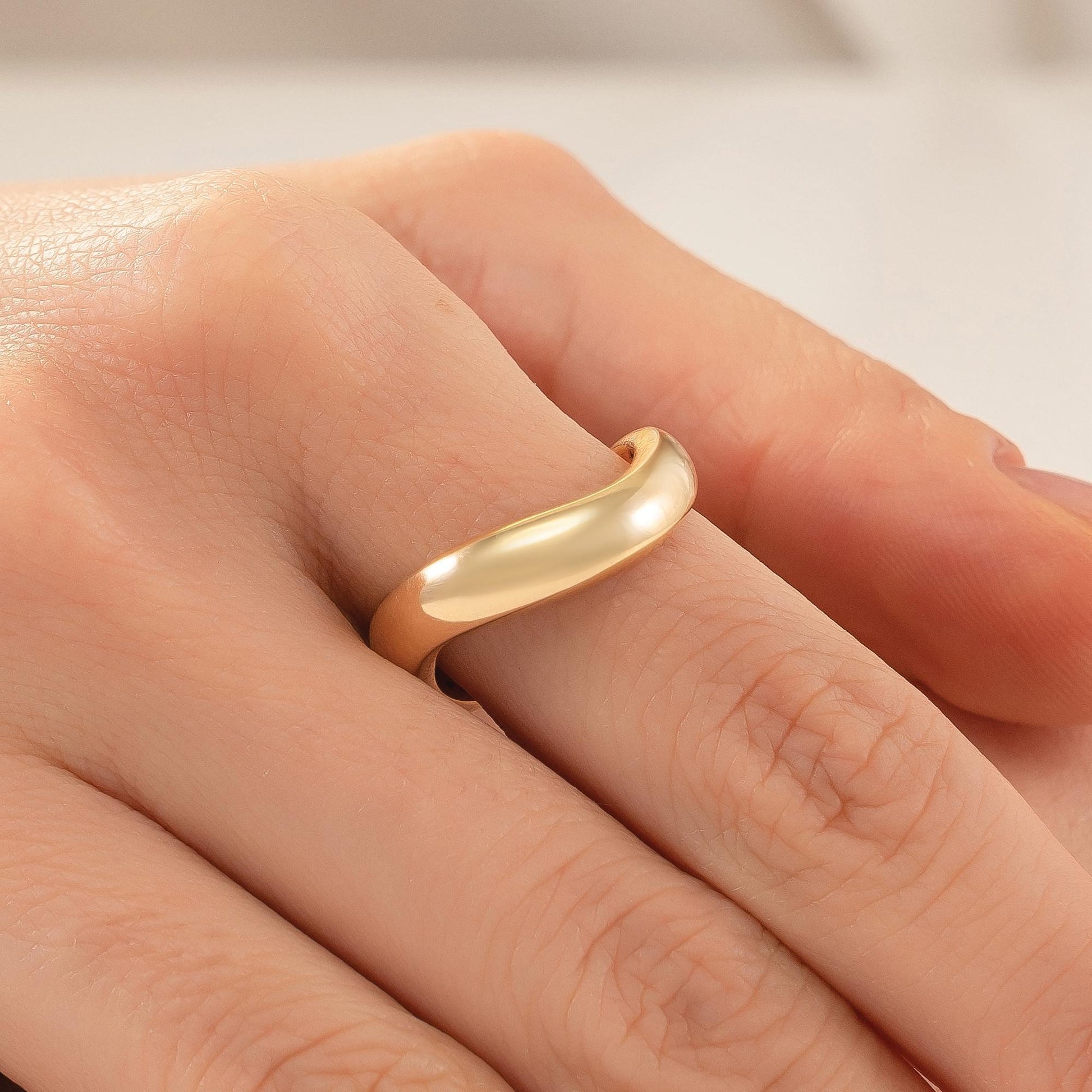 A close-up image of a person's hand wearing a gold ring on the ring finger.
