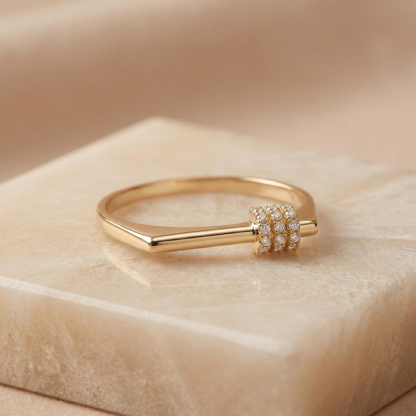A gold ring with a diamond accent sits on a marble surface.