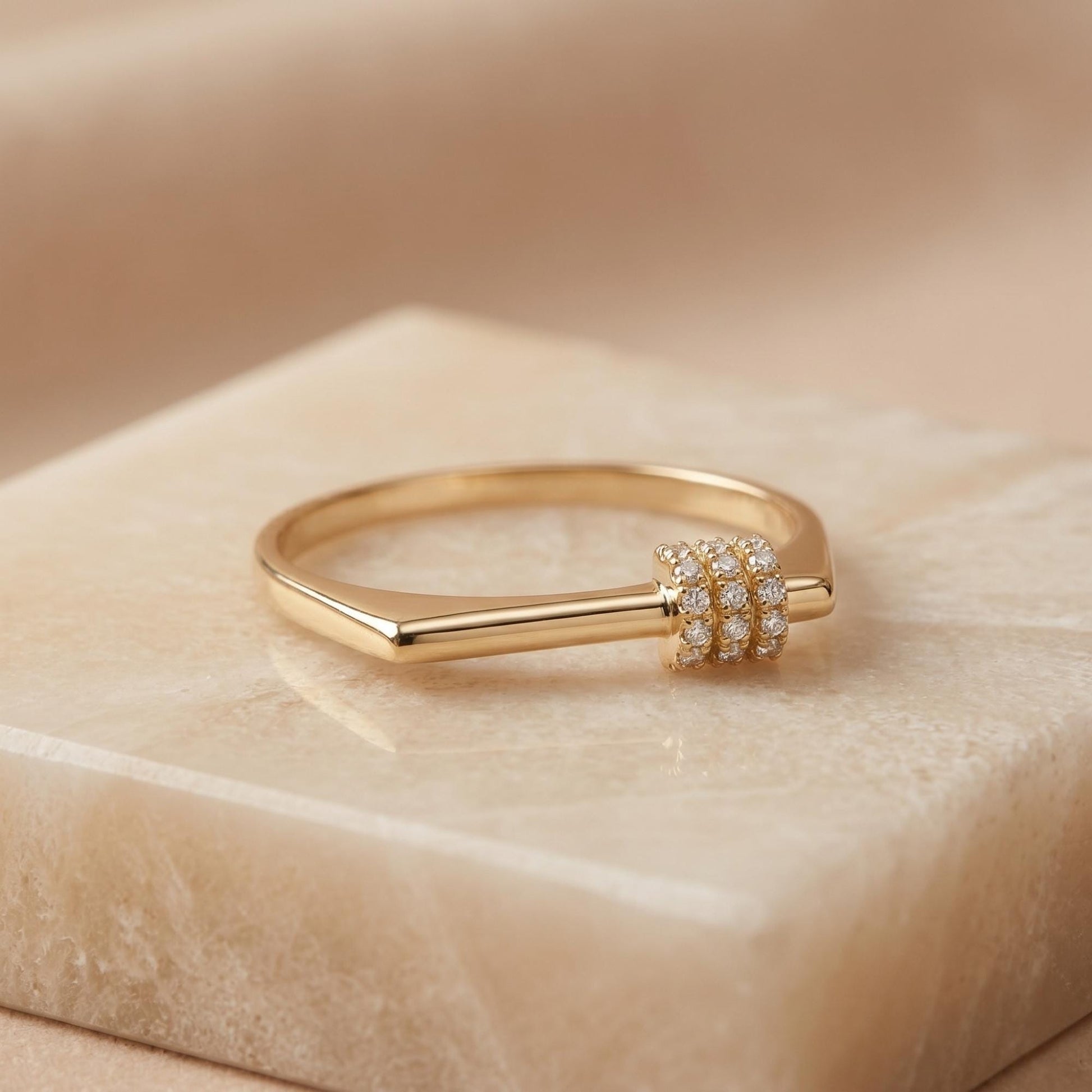 A gold ring with a diamond accent sits on a marble surface.