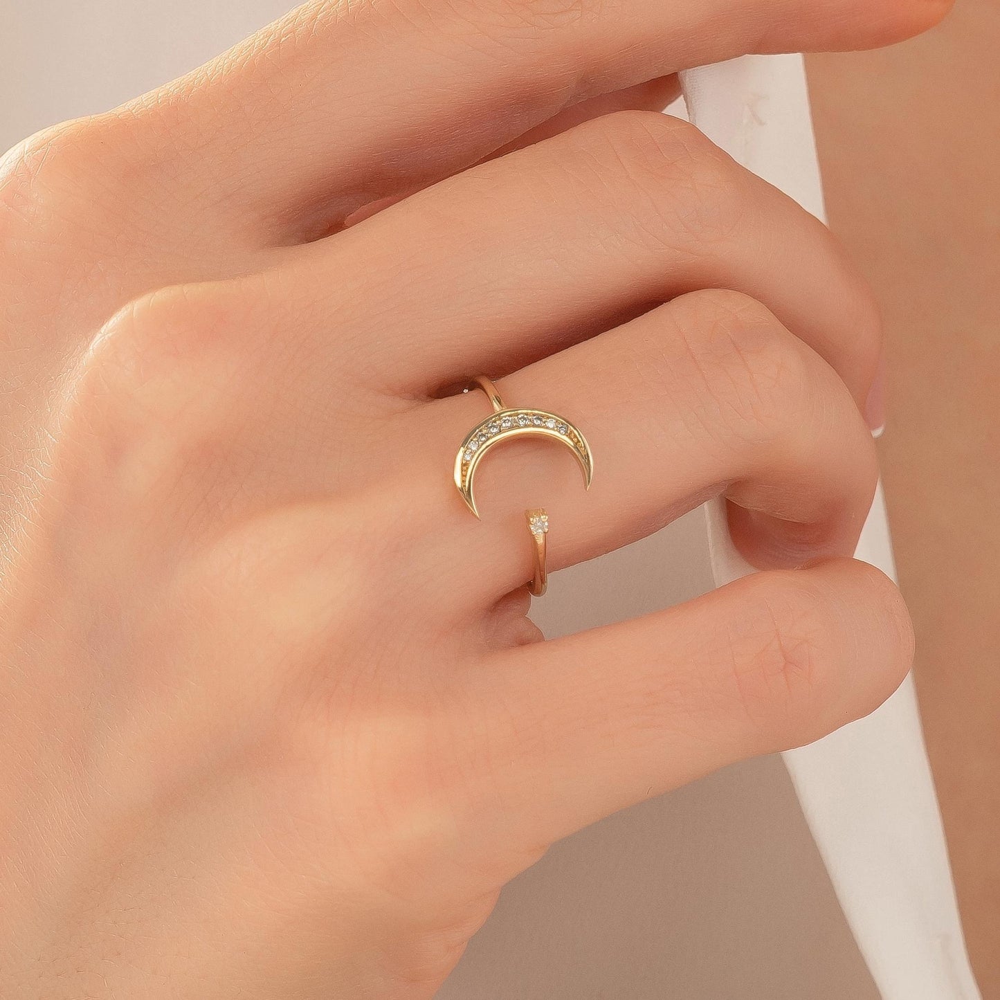 A close-up view of a person's hand wearing a gold ring with a crescent moon design.
