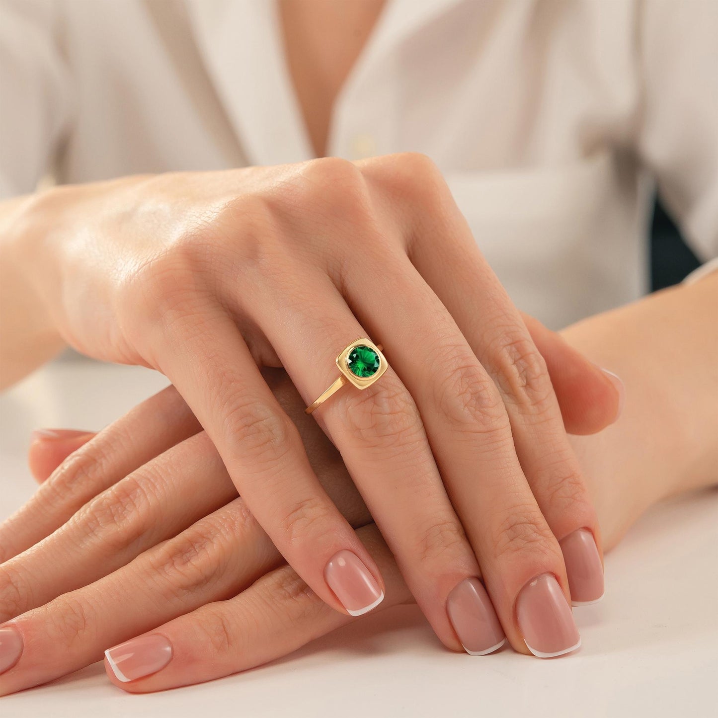 A close-up image of a person's hands wearing a gold ring with a green gemstone.