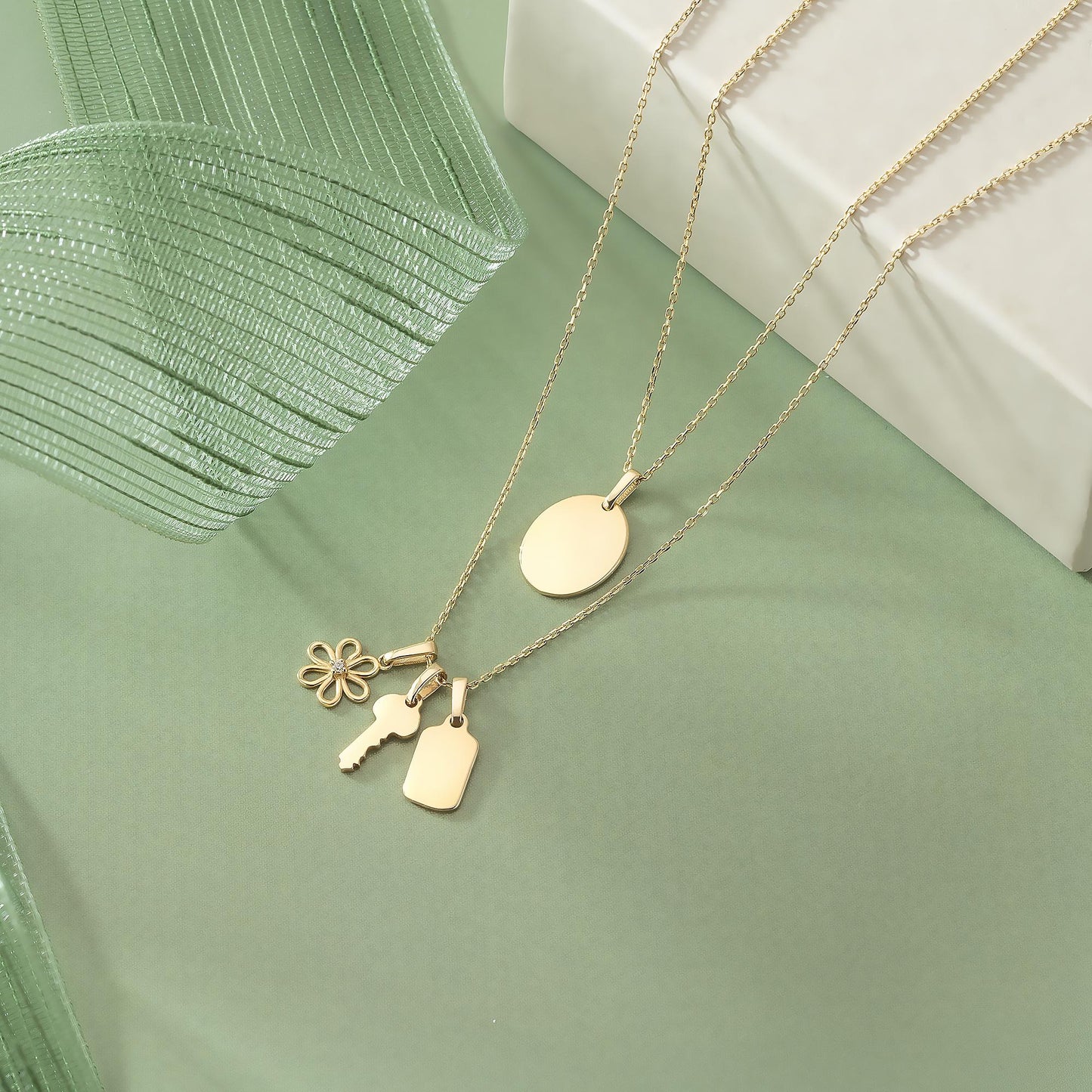A gold-colored necklace with various charms, including a key, flower, and tag, is displayed on a green background.