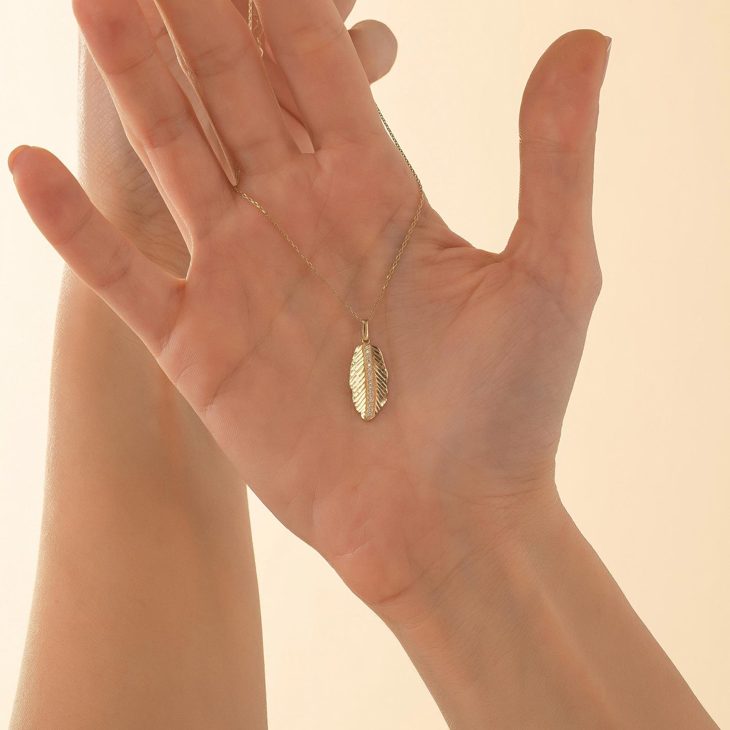 A close-up image of a person's hand holding a gold necklace with a leaf-shaped pendant.