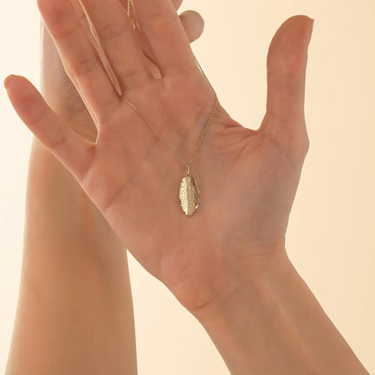 A close-up image of a person's hand holding a gold necklace with a leaf-shaped pendant.