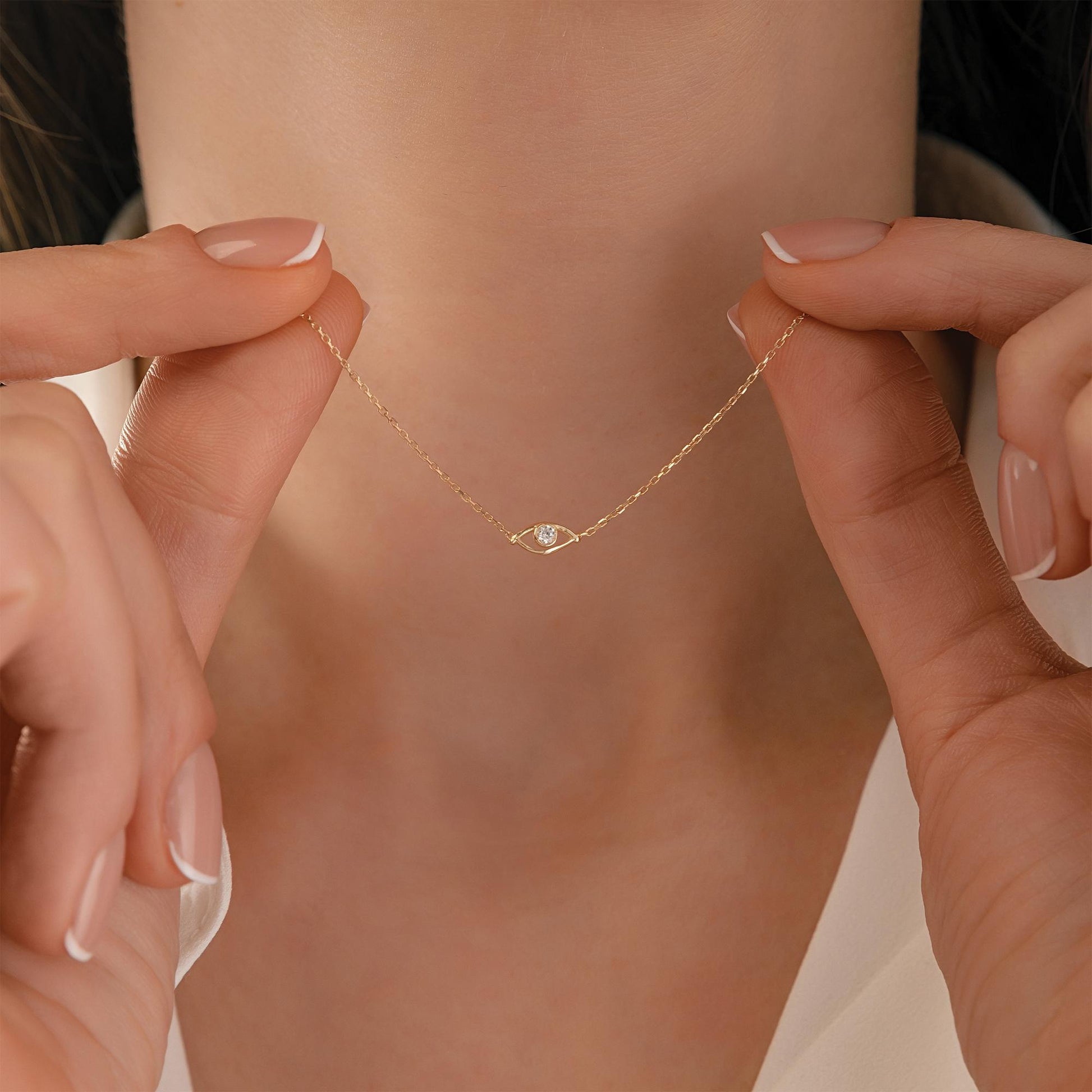 A close-up of a person's hands holding a delicate gold necklace with a small diamond pendant.