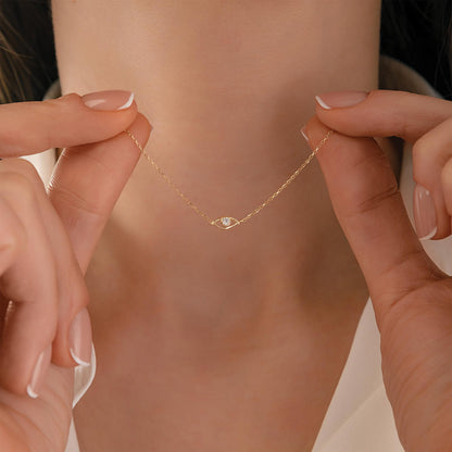 A close-up of a person's hands holding a delicate gold necklace with a small diamond pendant.