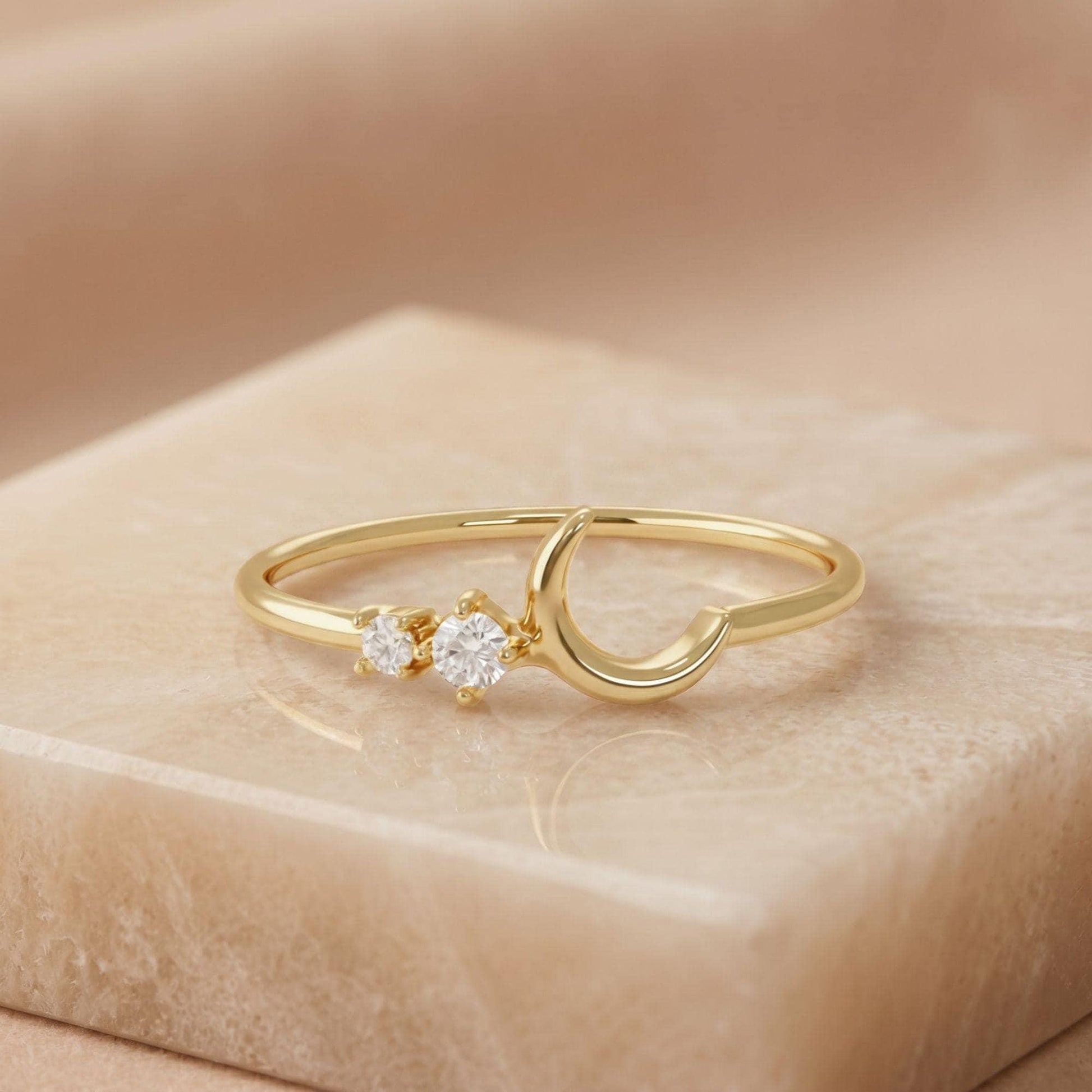 A gold ring with a crescent moon design and two small diamonds on the band.
