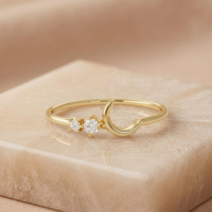 A gold ring with a crescent moon design and two small diamonds on the band.