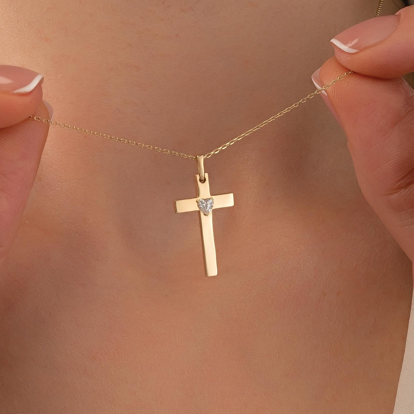 A person's hand holding a gold cross pendant necklace.