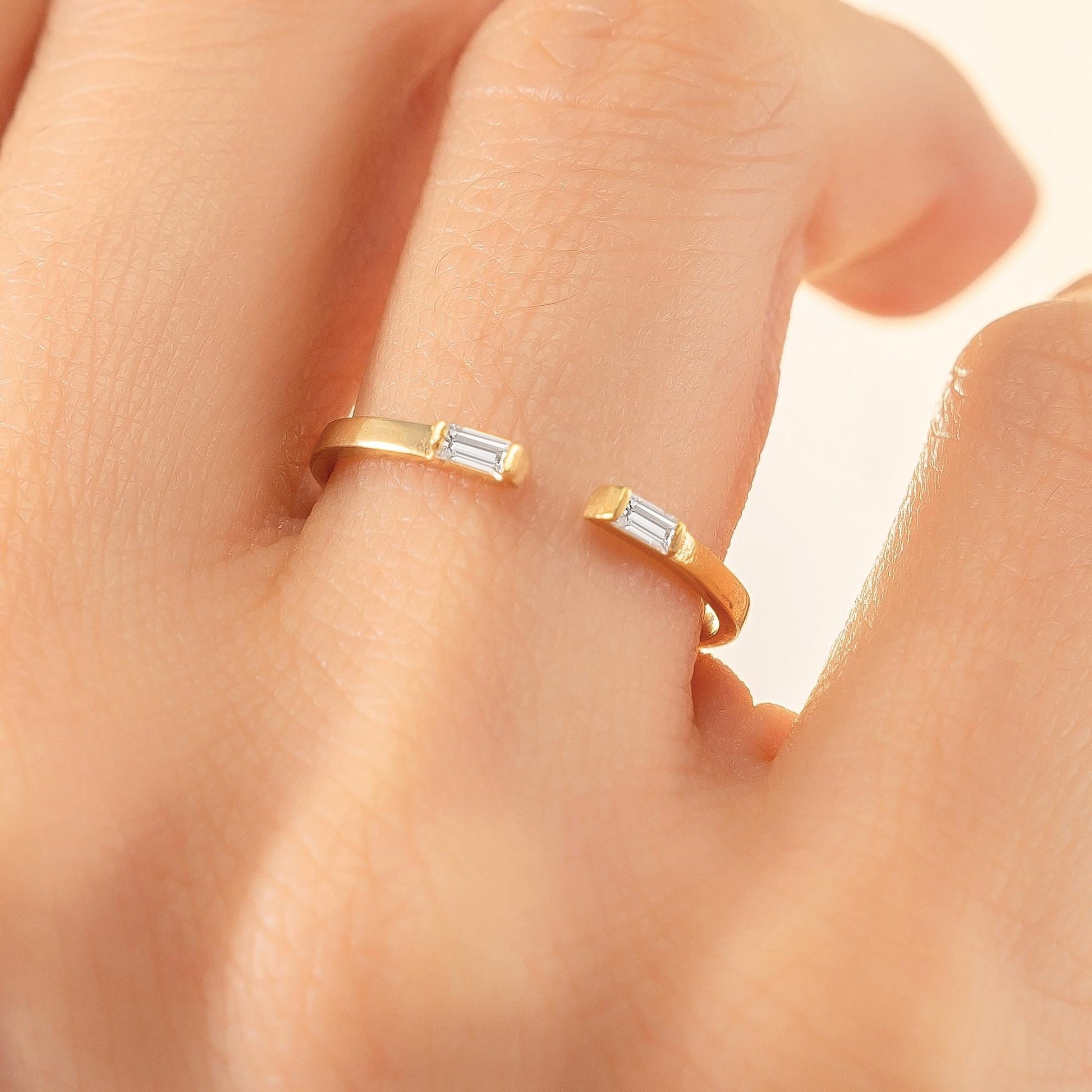 A close-up of a person's hand wearing a gold ring with two diamond-like stones.