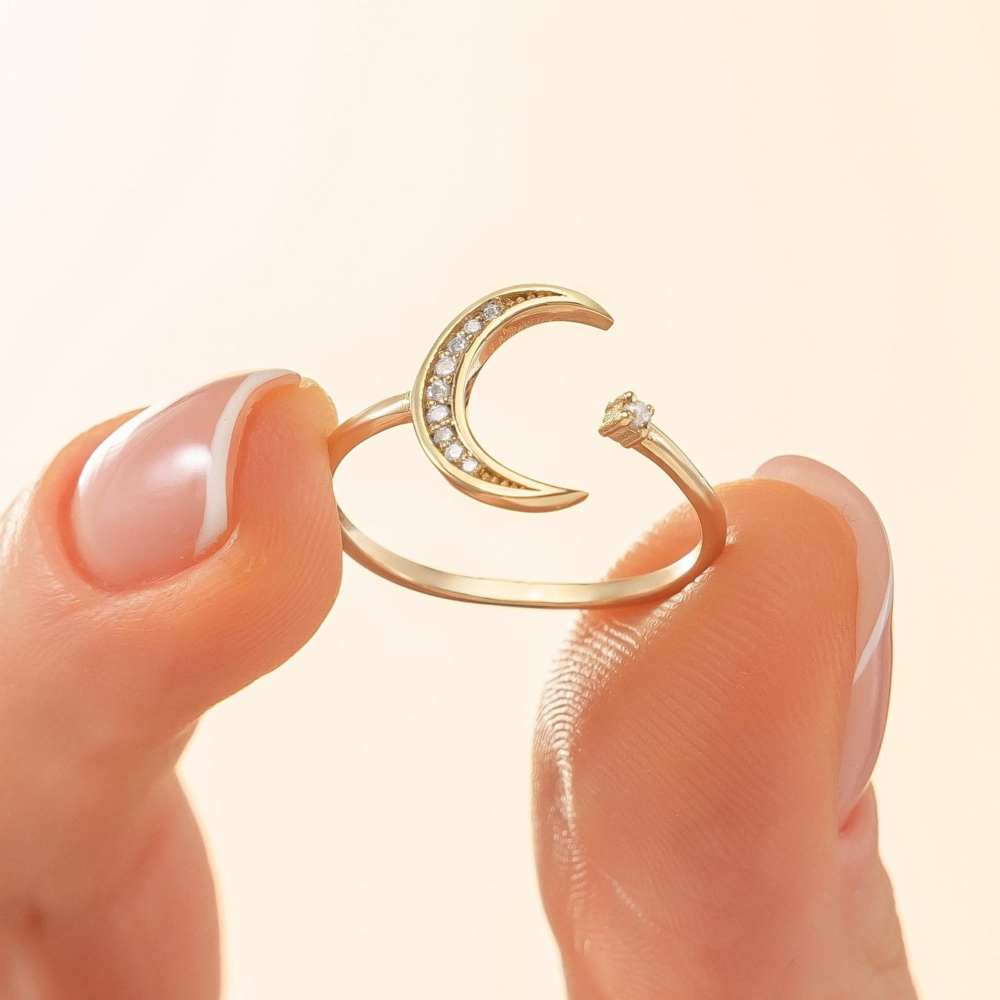 A gold ring with a crescent moon design and small diamonds is being held between two fingers.