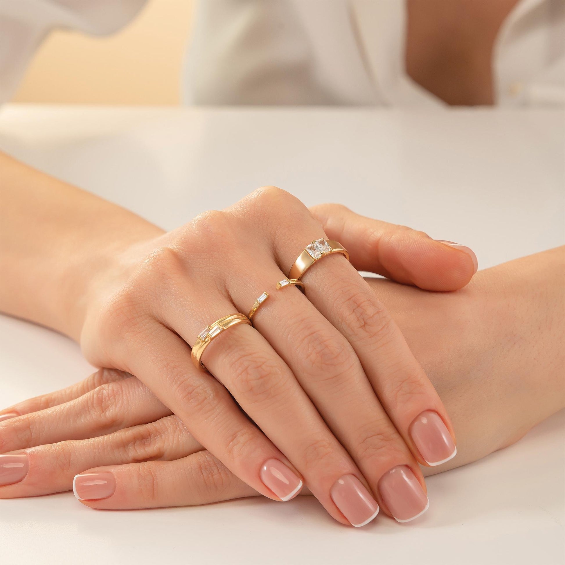 A close-up image of a person's hands wearing three gold rings on their fingers.