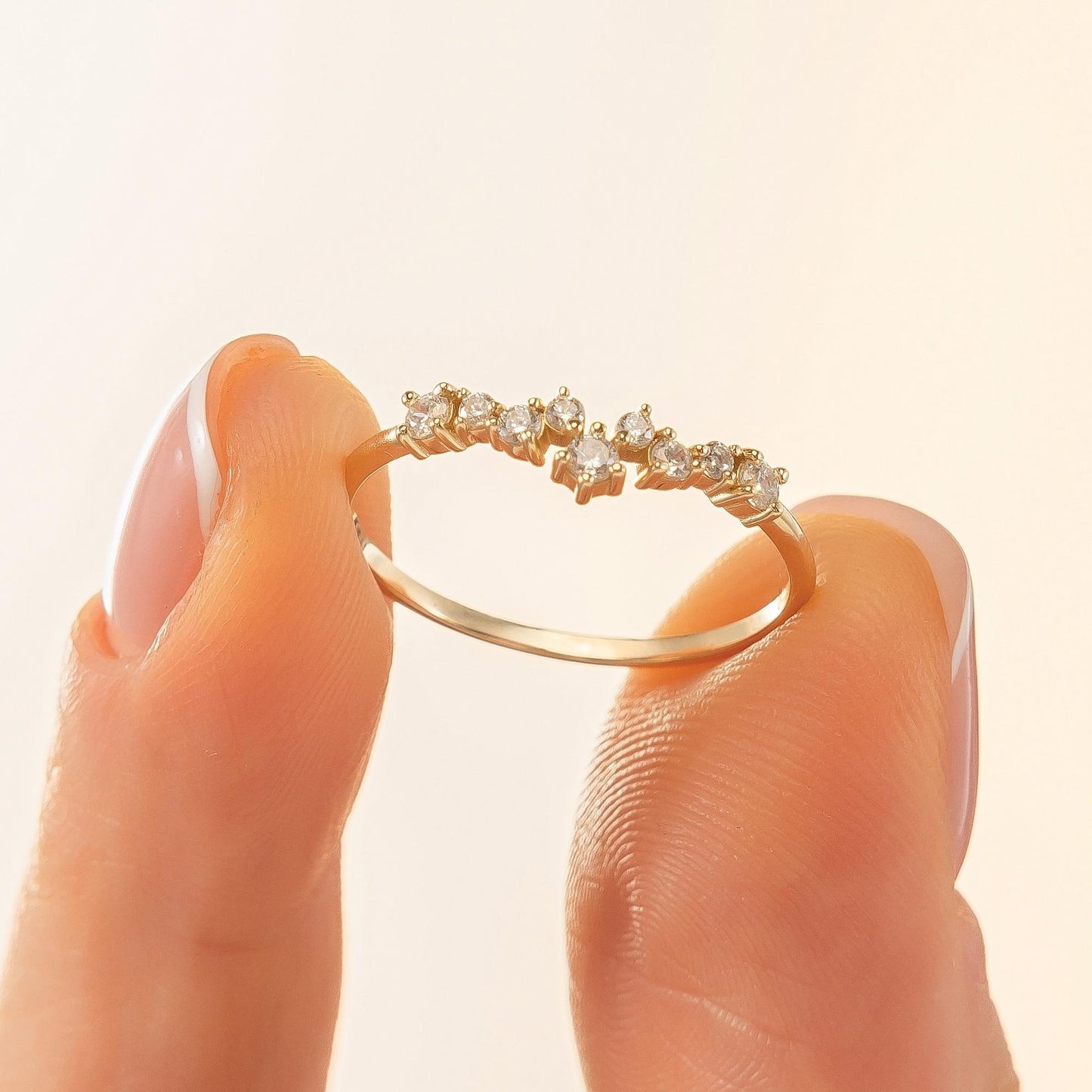A close-up image of a person's fingers holding a gold ring with small diamonds on it.