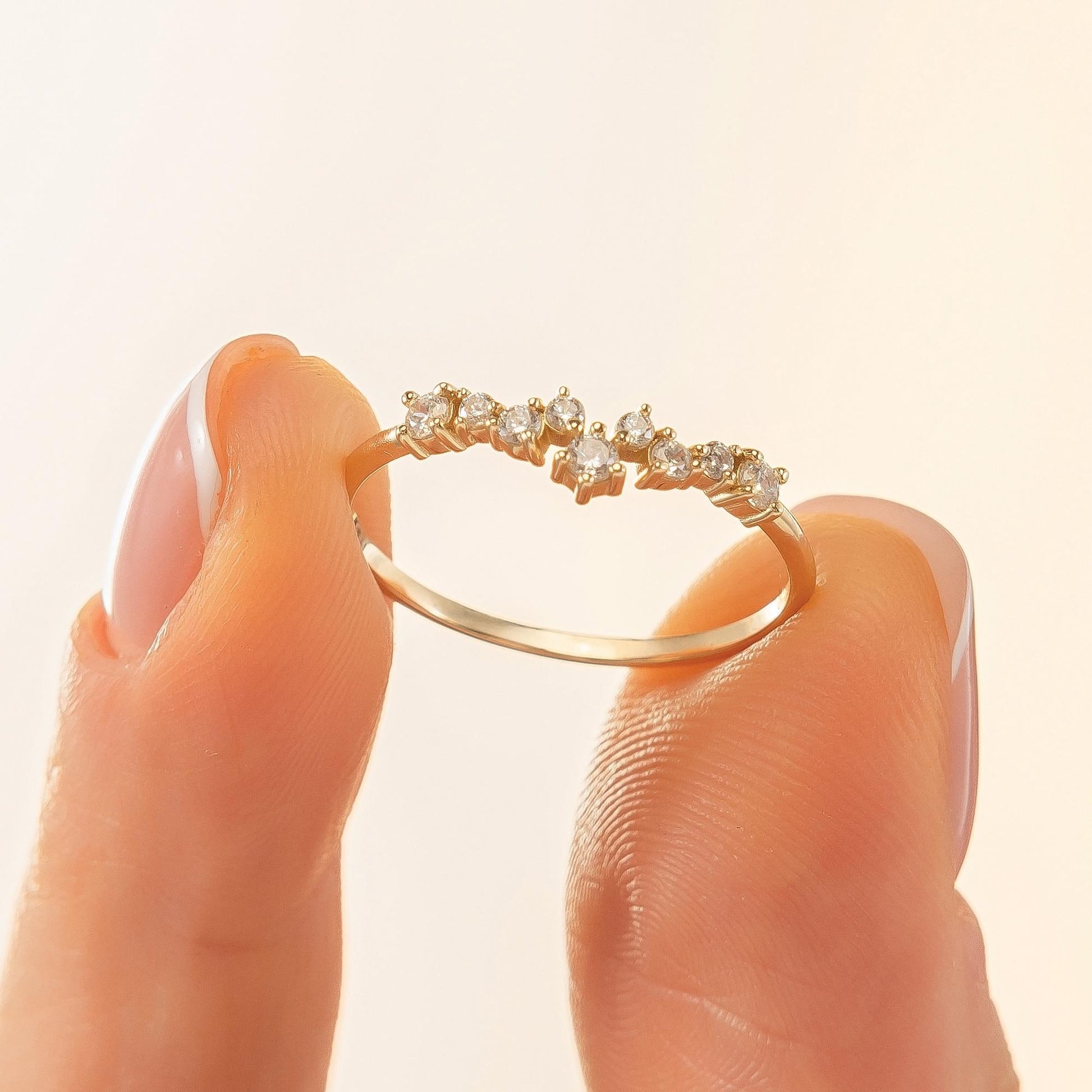 A close-up image of a person's fingers holding a gold ring with small diamonds on it.