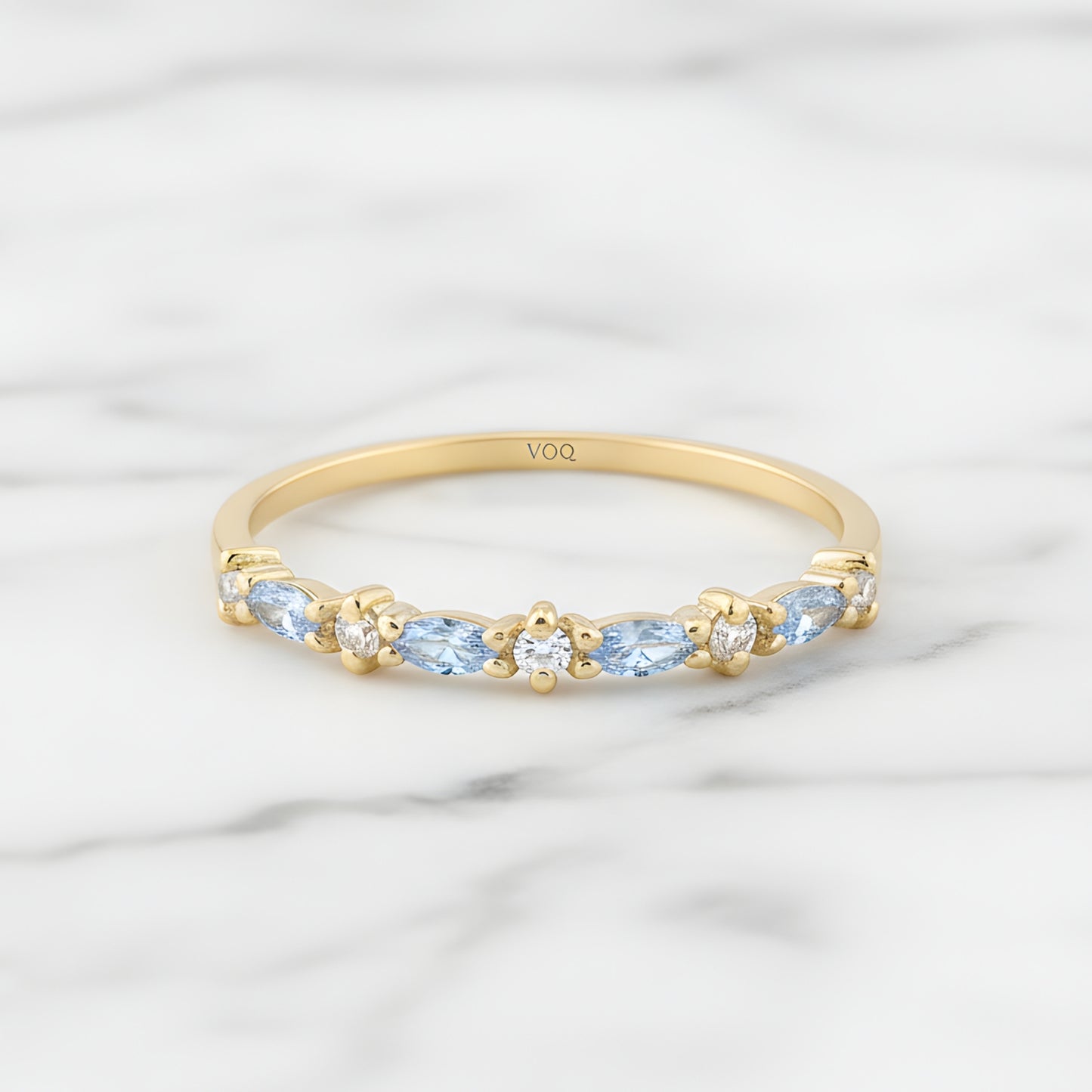 A gold ring with blue gemstones set in a row, placed on a marble surface.