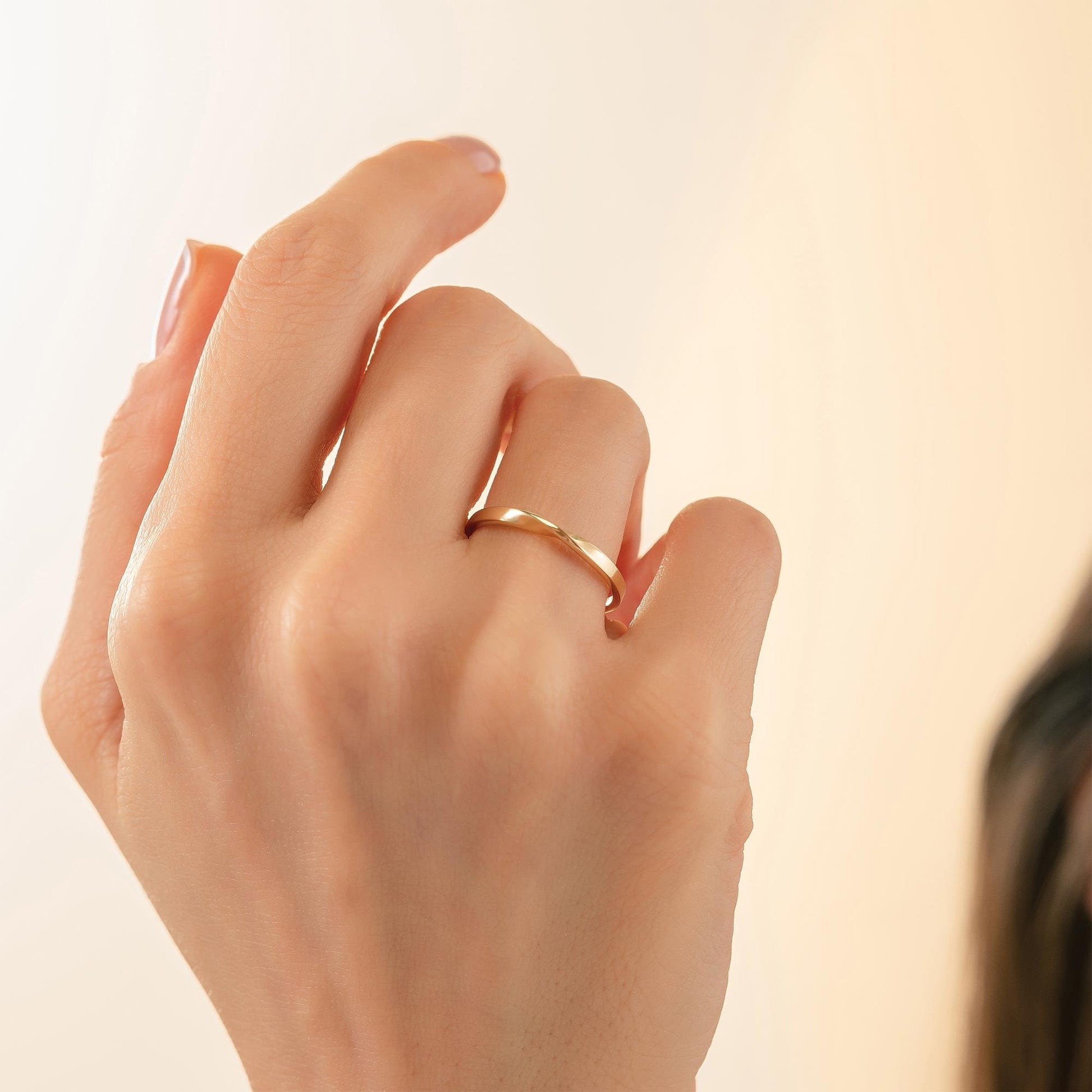 A close-up of a person's hand wearing a gold ring, with a blurred background.