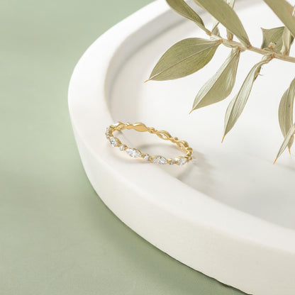 A gold ring with a diamond-encrusted band is displayed on a white surface, with a branch of green leaves in the background.