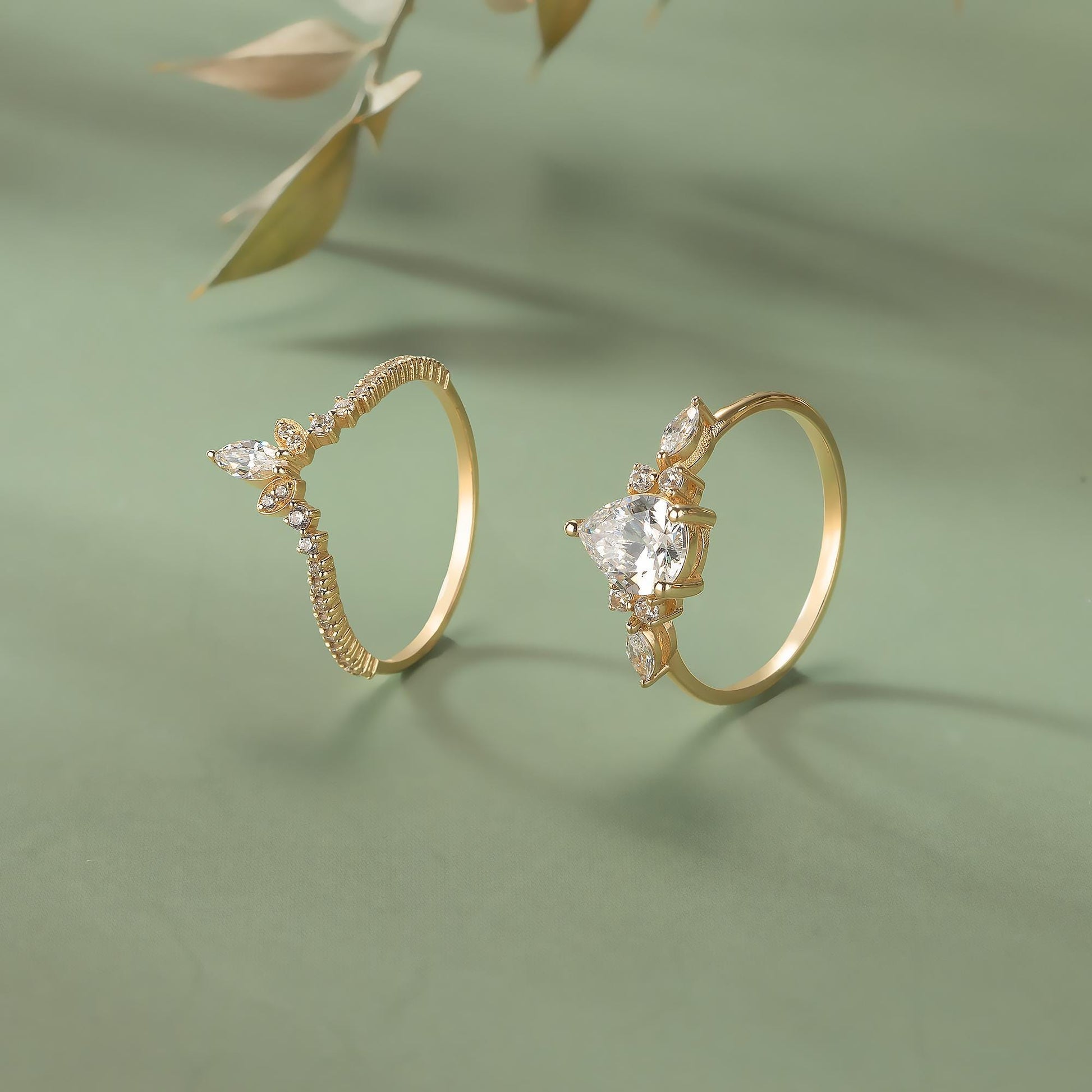 Two gold rings with diamond accents are displayed on a green background.