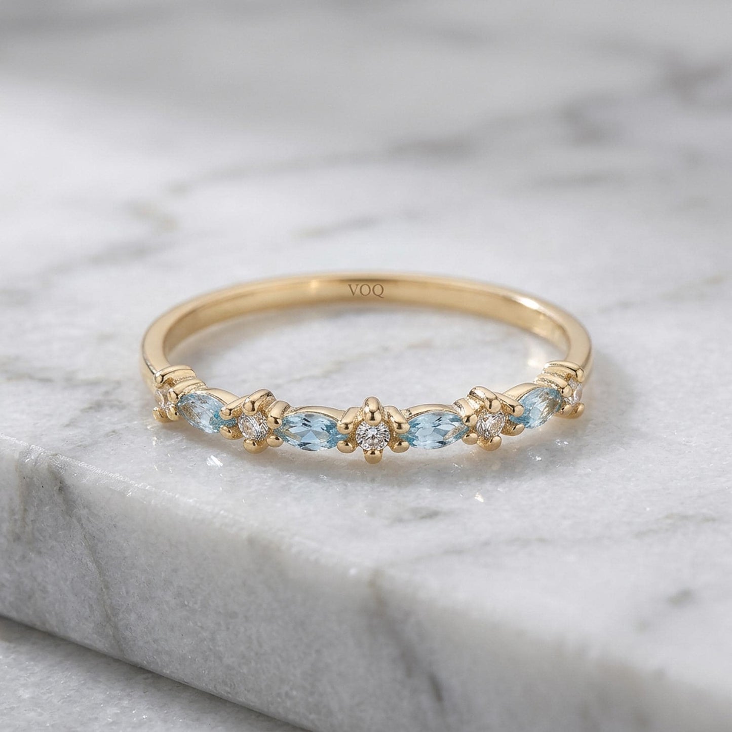 A gold ring with a row of blue gemstones, including aquamarine and diamonds, set in a band.