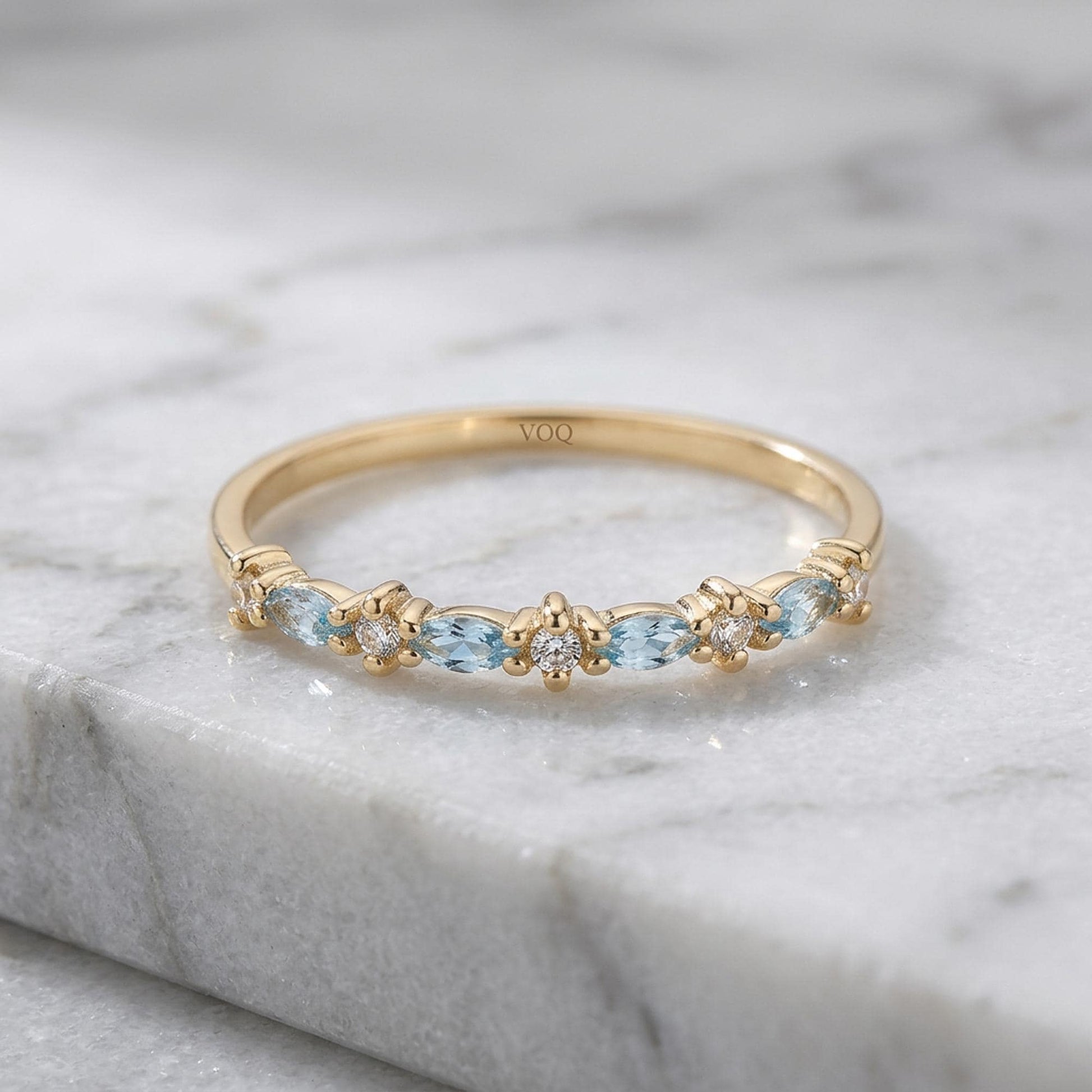 A gold ring with a row of blue gemstones, including aquamarine and diamonds, set in a band.