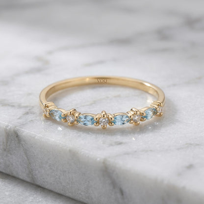 A gold ring with a row of blue gemstones, including aquamarine and diamonds, set in a band.
