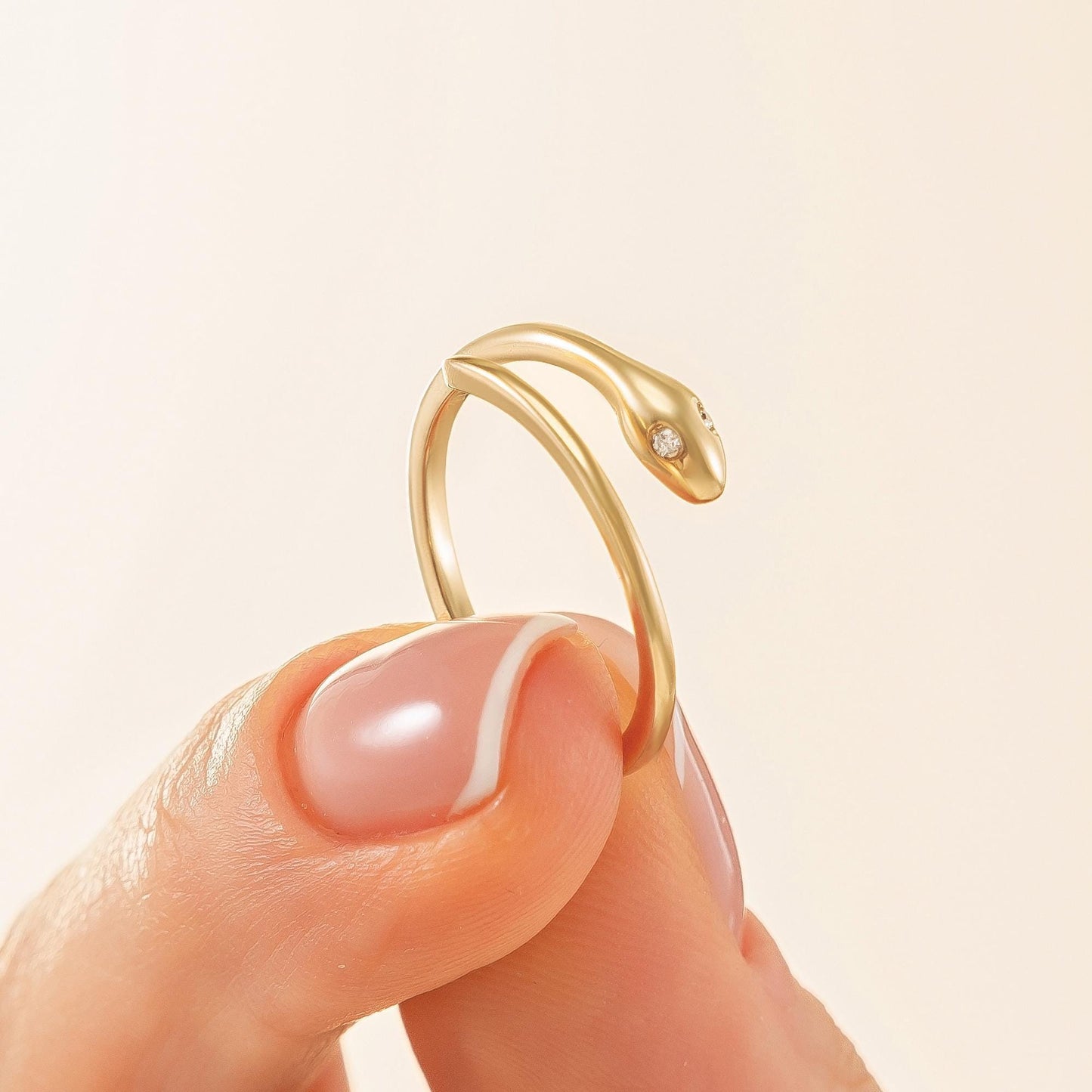 A gold ring with a snake design is being held in a person's hand against a light background.