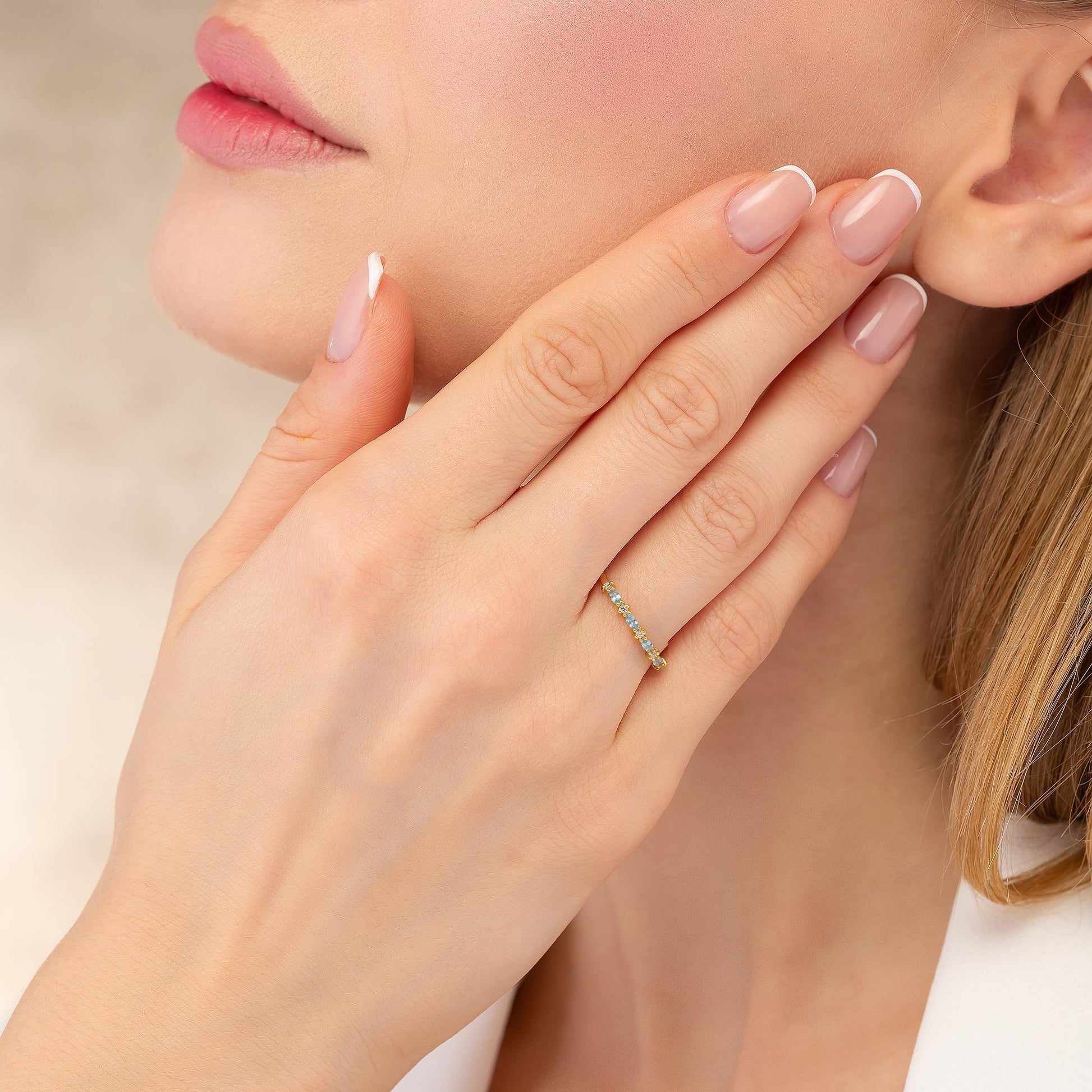 A close-up of a woman's hand wearing a ring, with her fingers gently resting on her face.