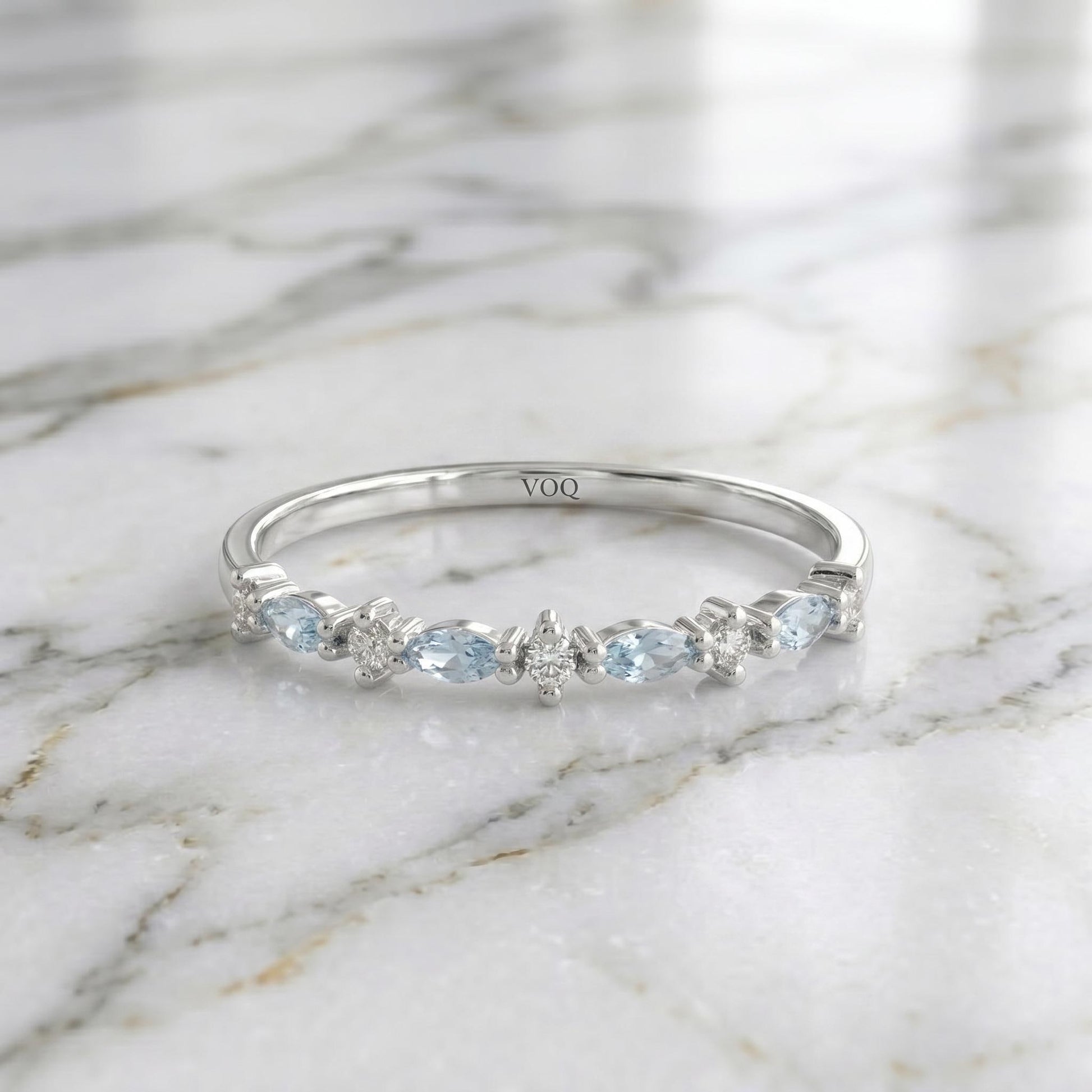 A silver ring with a row of blue gemstones, including aquamarine and diamonds, set in a band.