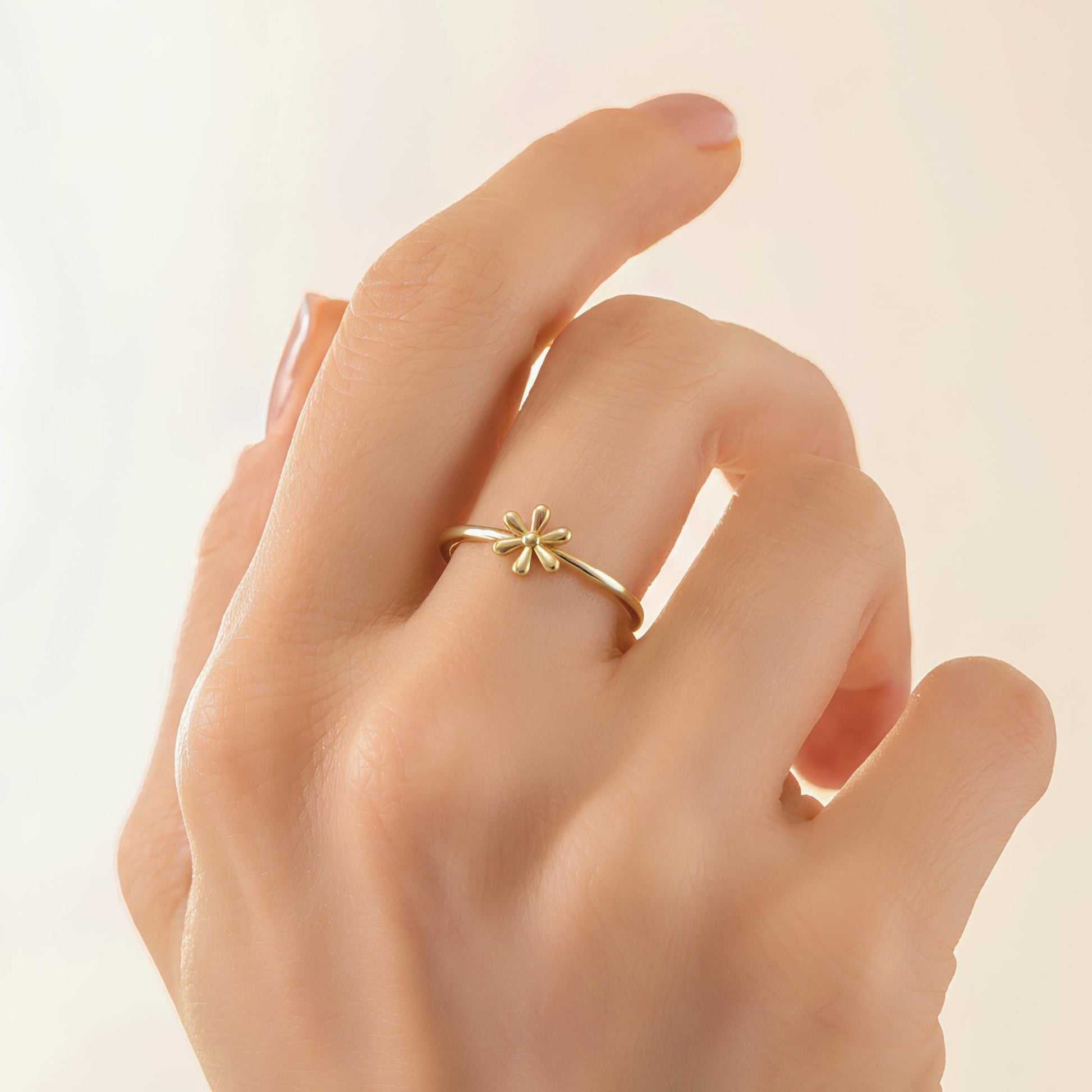 A close-up of a person's hand wearing a gold ring with a flower design.