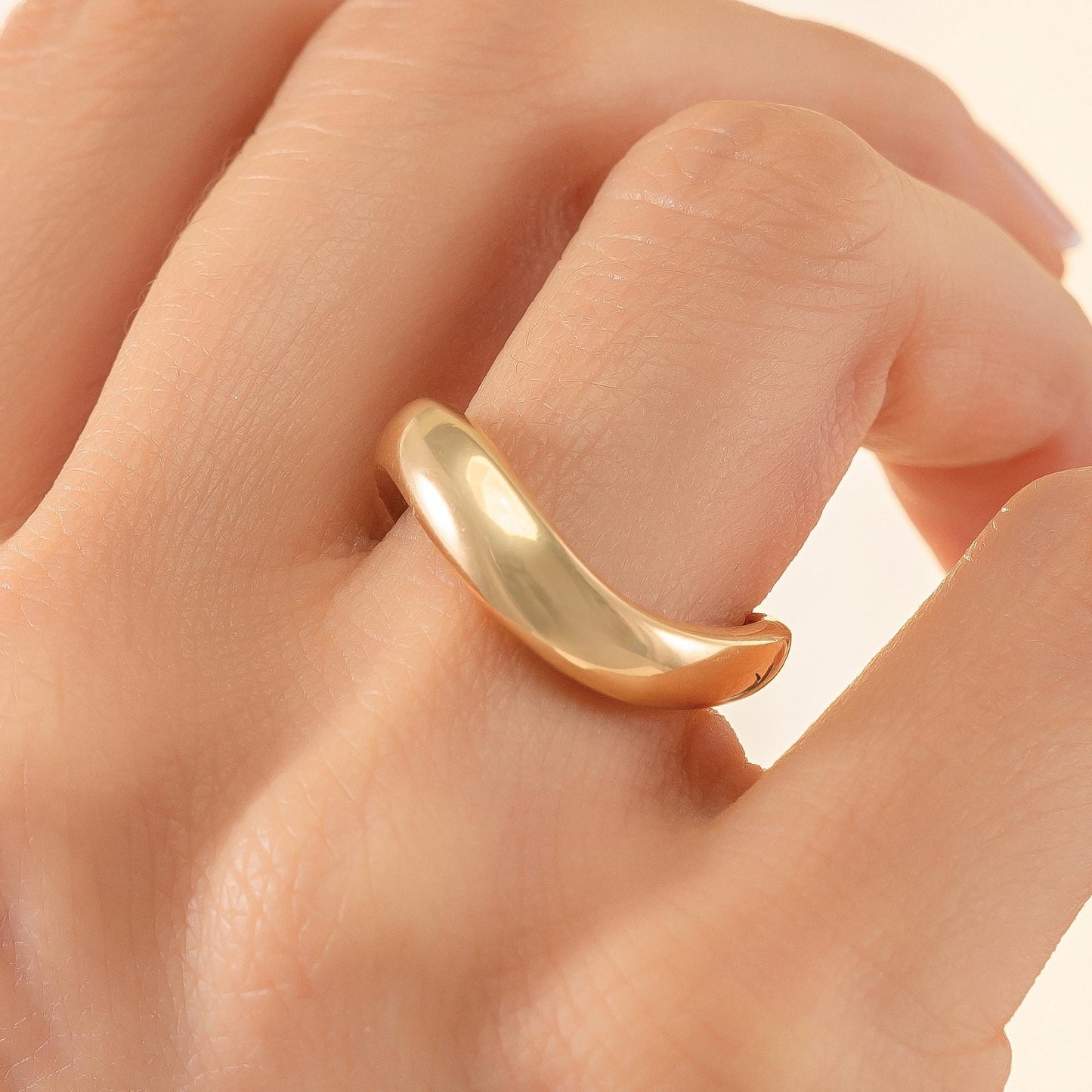 A close-up image of a person's hand wearing a gold ring on the ring finger.
