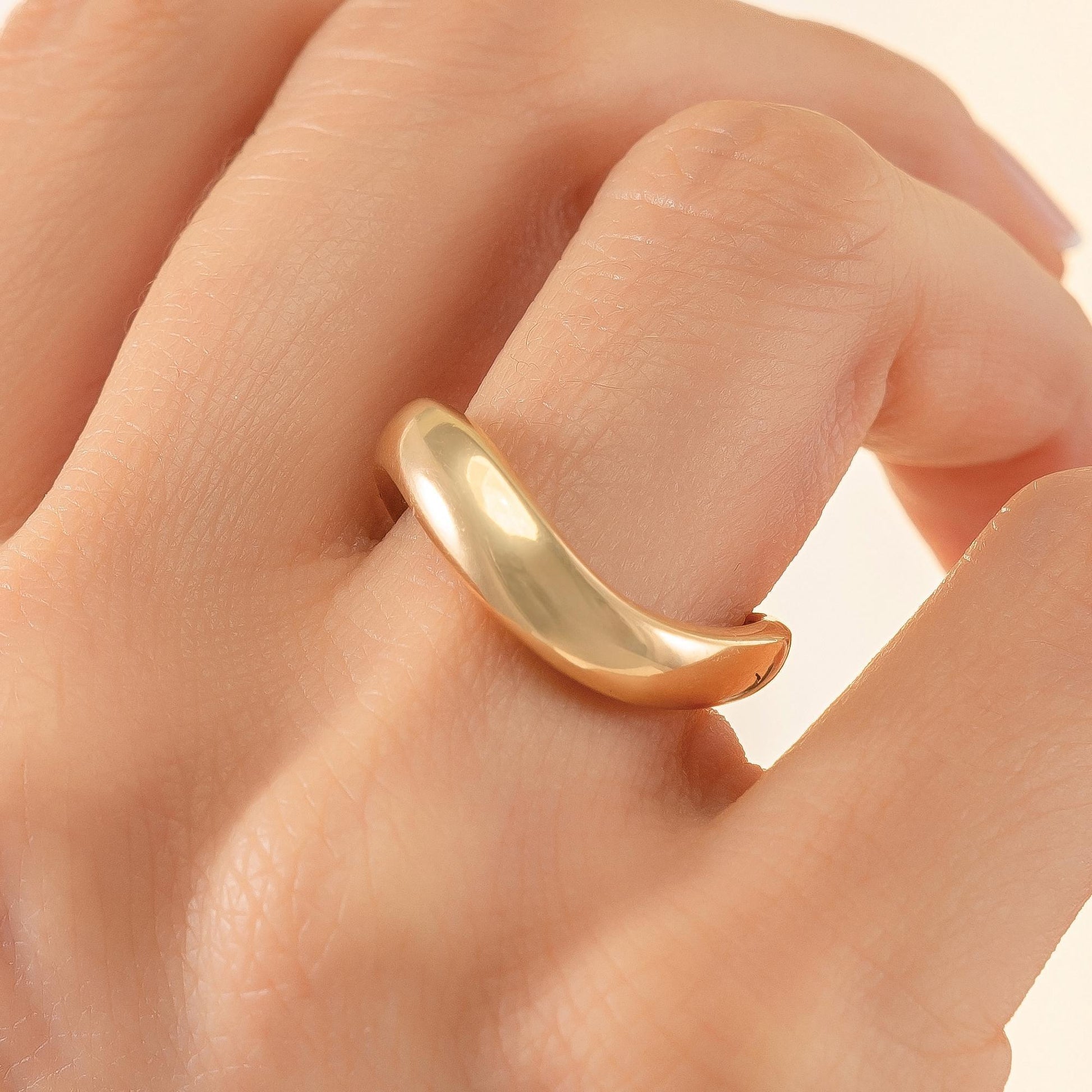 A close-up image of a person's hand wearing a gold ring on the ring finger.
