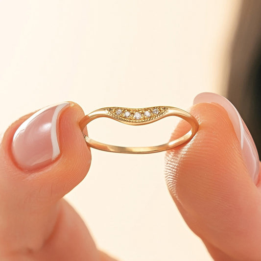 A close-up image of a person's fingers holding a gold ring with a diamond accent.