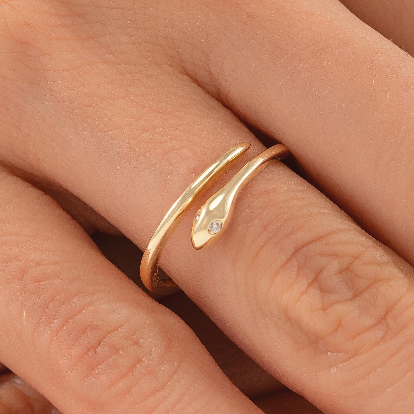A close-up image of a gold ring with a snake design on the finger.