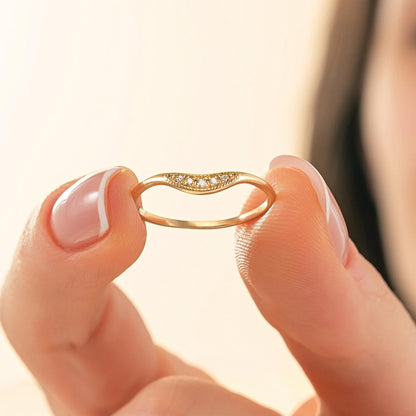 A person's hand holding a gold ring with a small diamond accent.