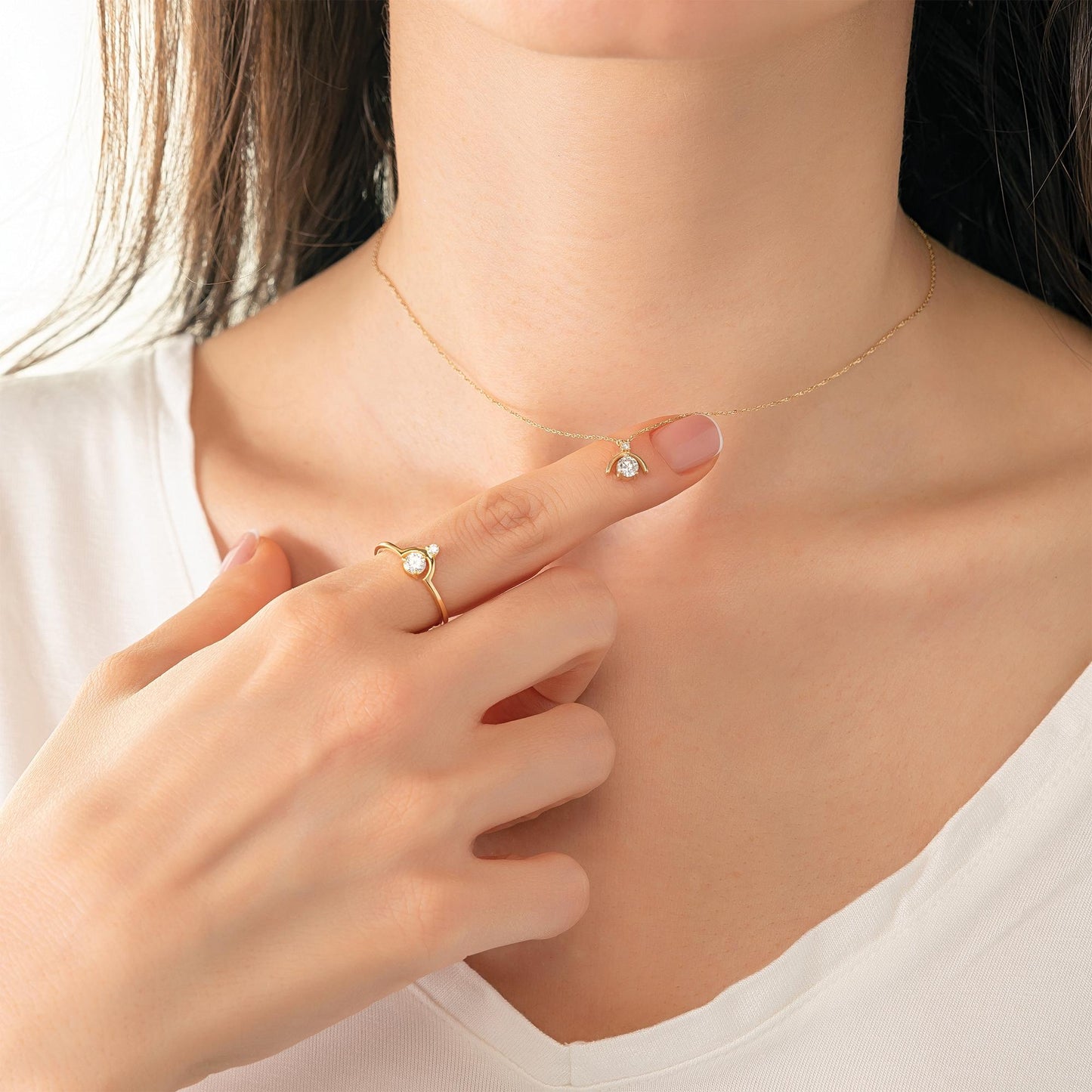 A close-up of a person's hand wearing a gold necklace and ring, with the hand holding the ring up to the camera.