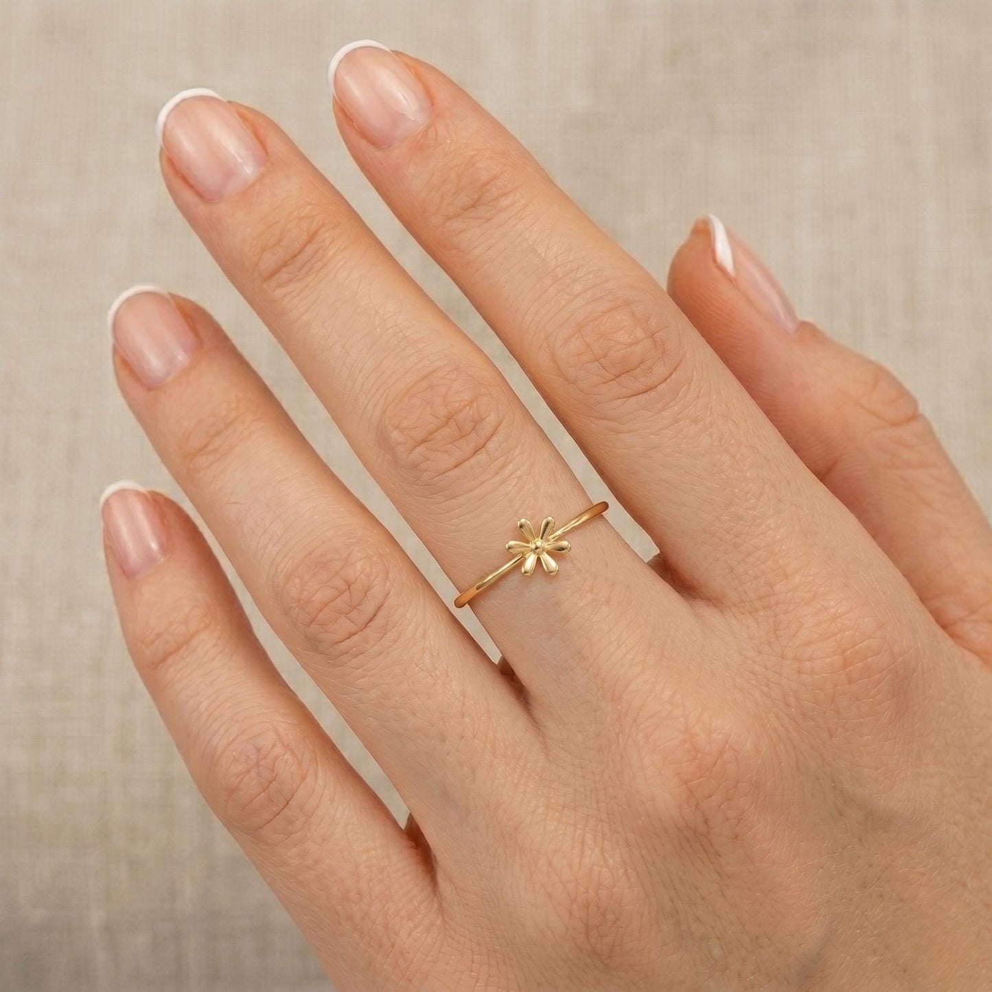 A close-up of a person's hand wearing a gold ring with a small flower design.