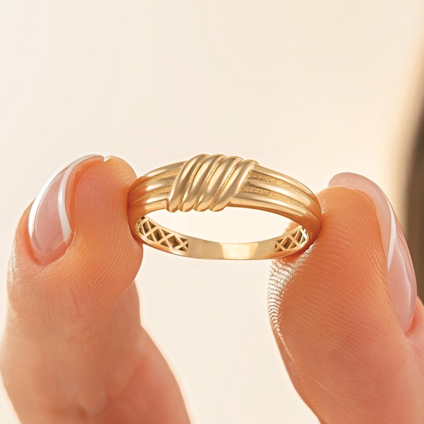 A close-up image of a person's hand holding a gold ring with a decorative band.