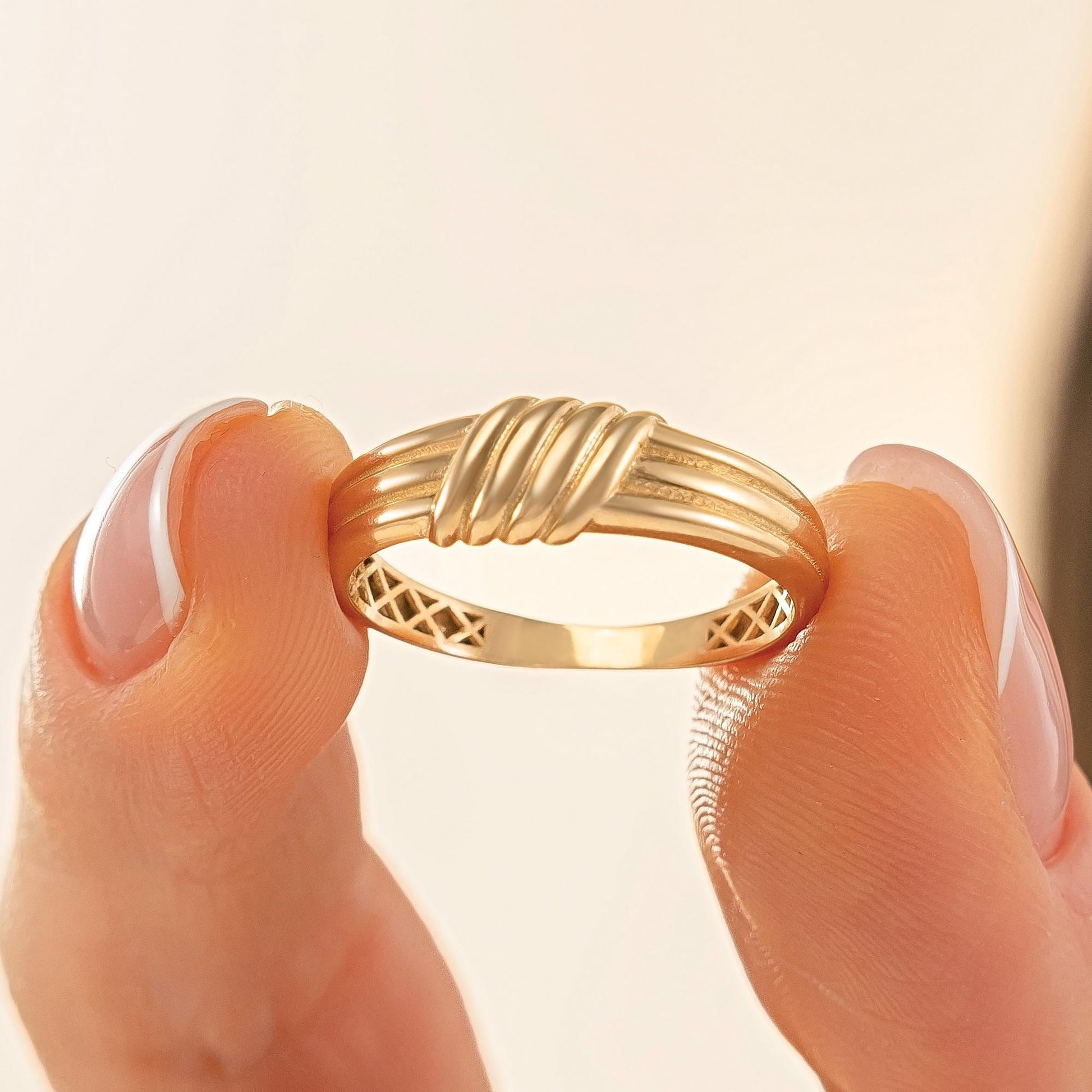 A close-up image of a person's hand holding a gold ring with a decorative band.