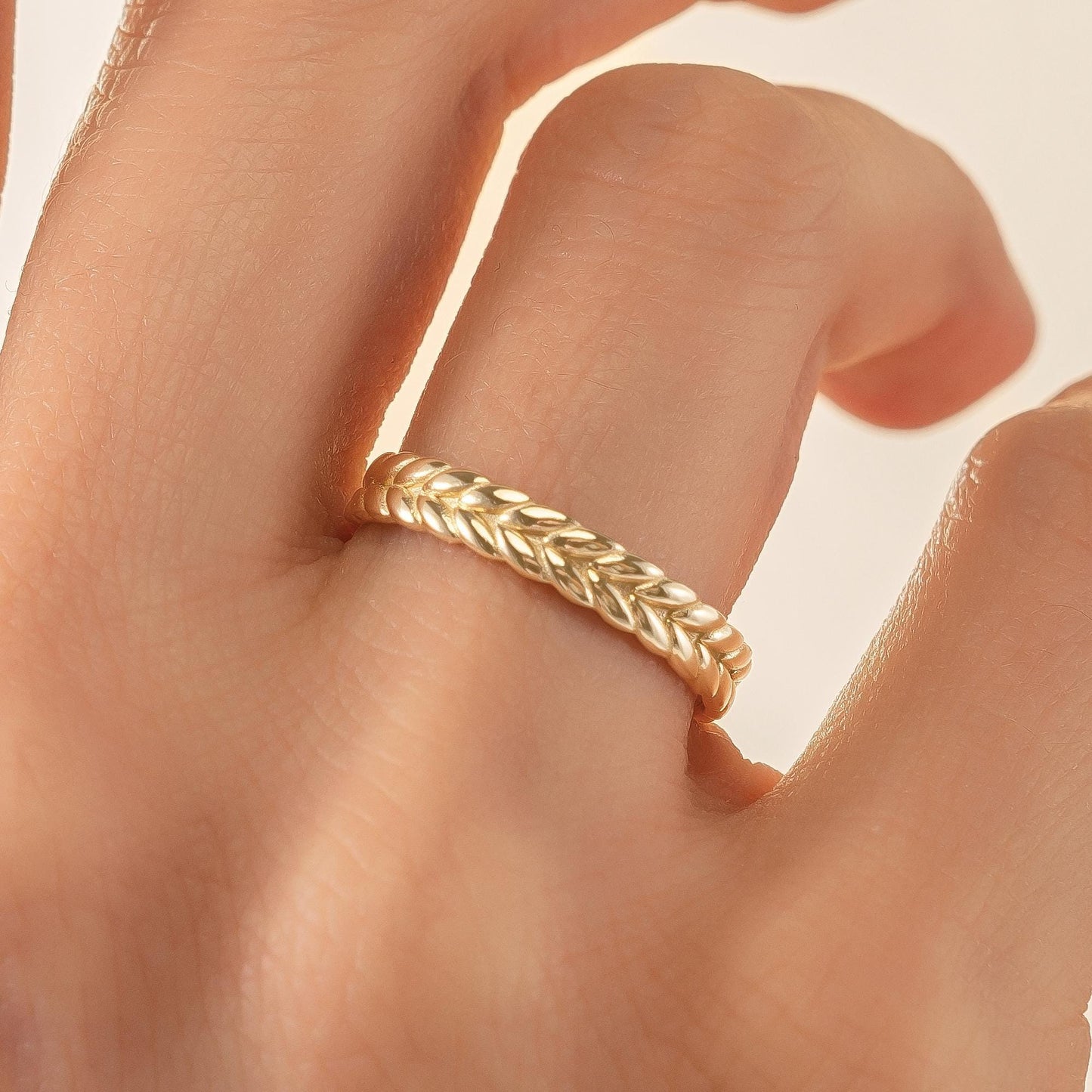 A gold ring with a braided band is shown on a person's hand.