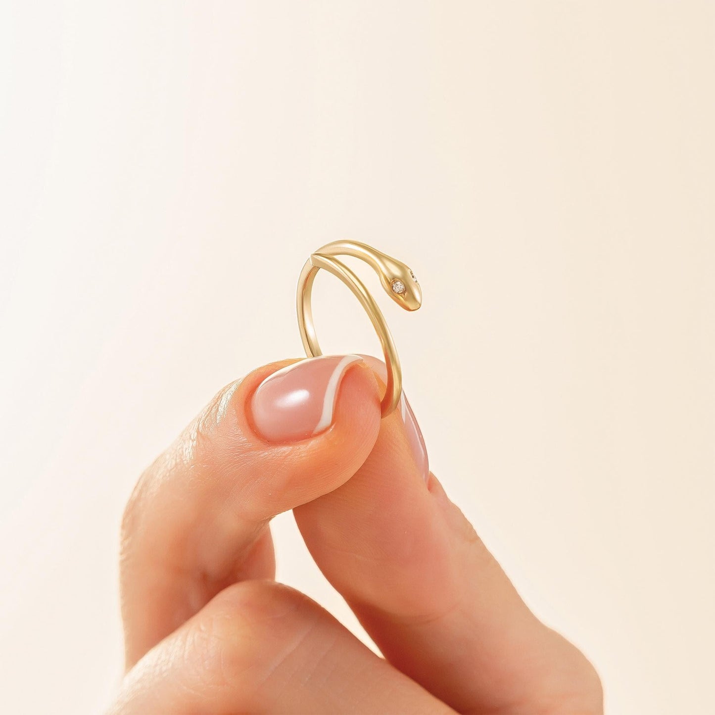 A close-up image of a person's hand holding a gold ring with a snake design.