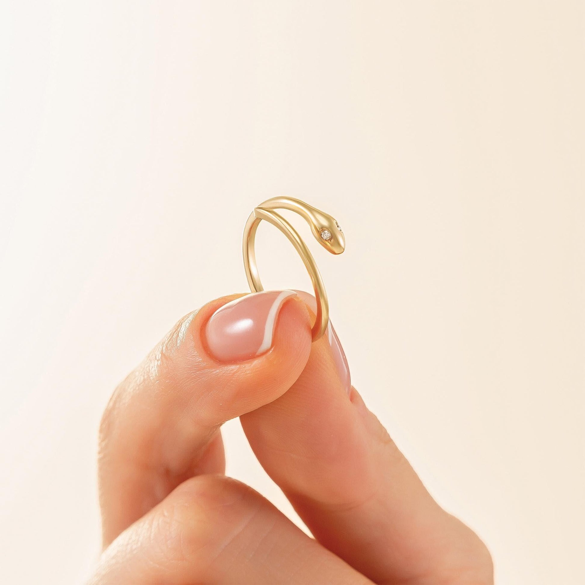 A close-up image of a person's hand holding a gold ring with a snake design.