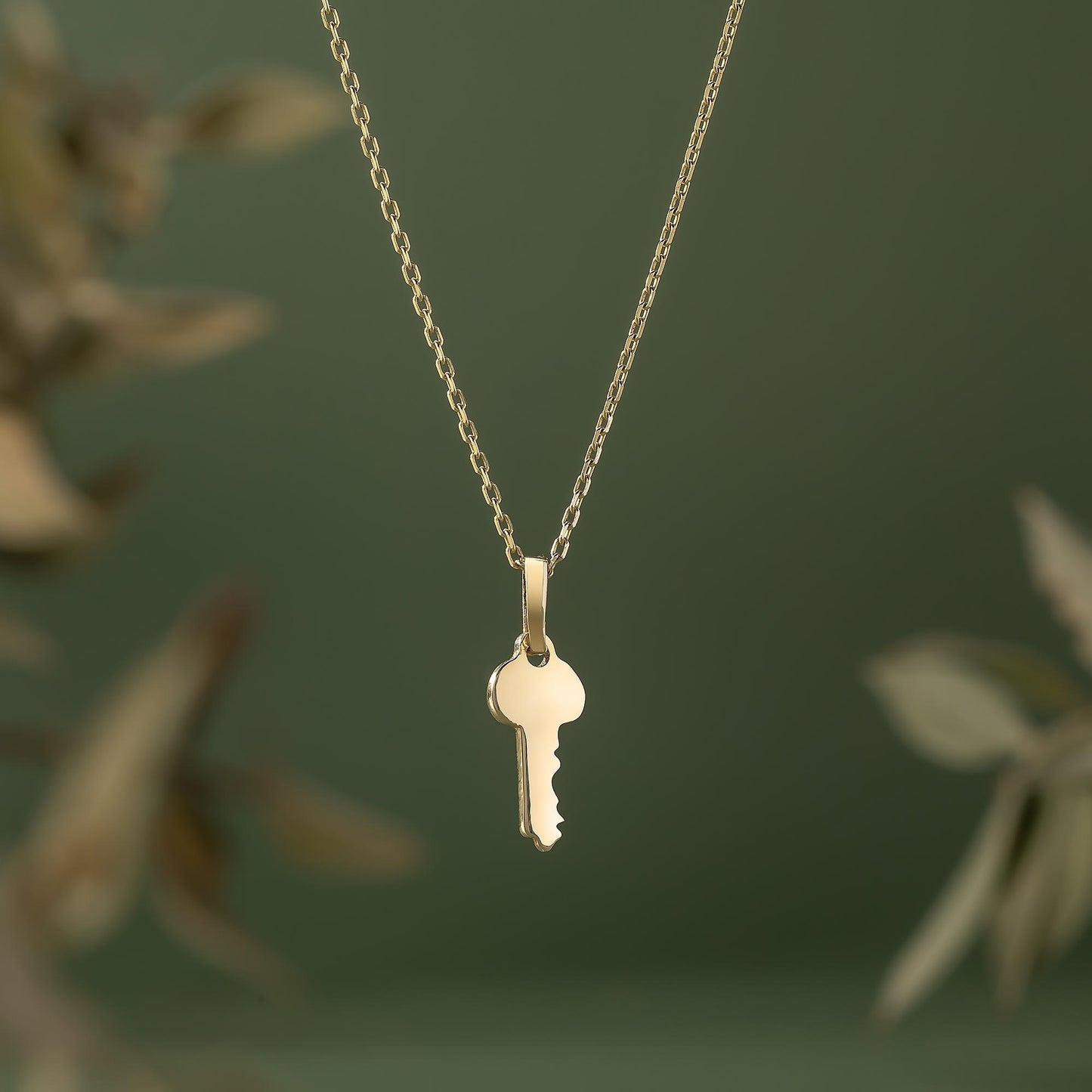 A gold-colored necklace with a small key pendant is shown against a blurred green background.