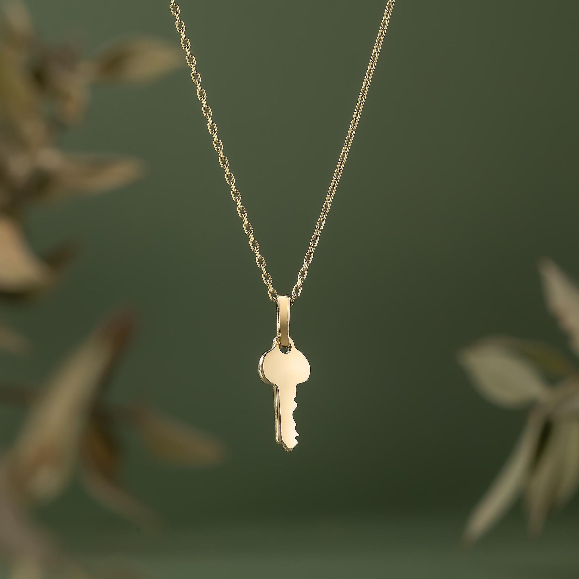 A gold-colored necklace with a small key pendant is shown against a blurred green background.