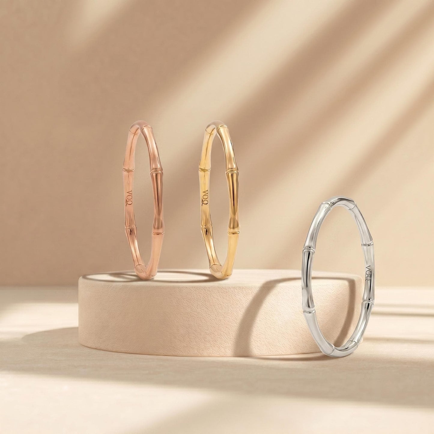Three gold-colored bracelets are displayed on a beige pedestal against a light beige background.