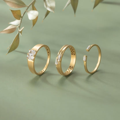 Three gold rings with gemstones are displayed against a green background, with a branch of leaves in the background.